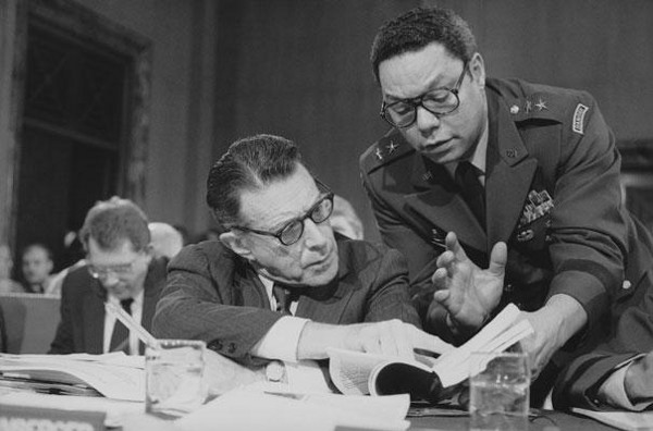Defense Secretary Caspar Weinberger speaks with Army Maj. Gen. Colin Powell during testimony before the Senate Budget Committee on Capitol Hill on Feb. 8, 1985. (AP Photo)
