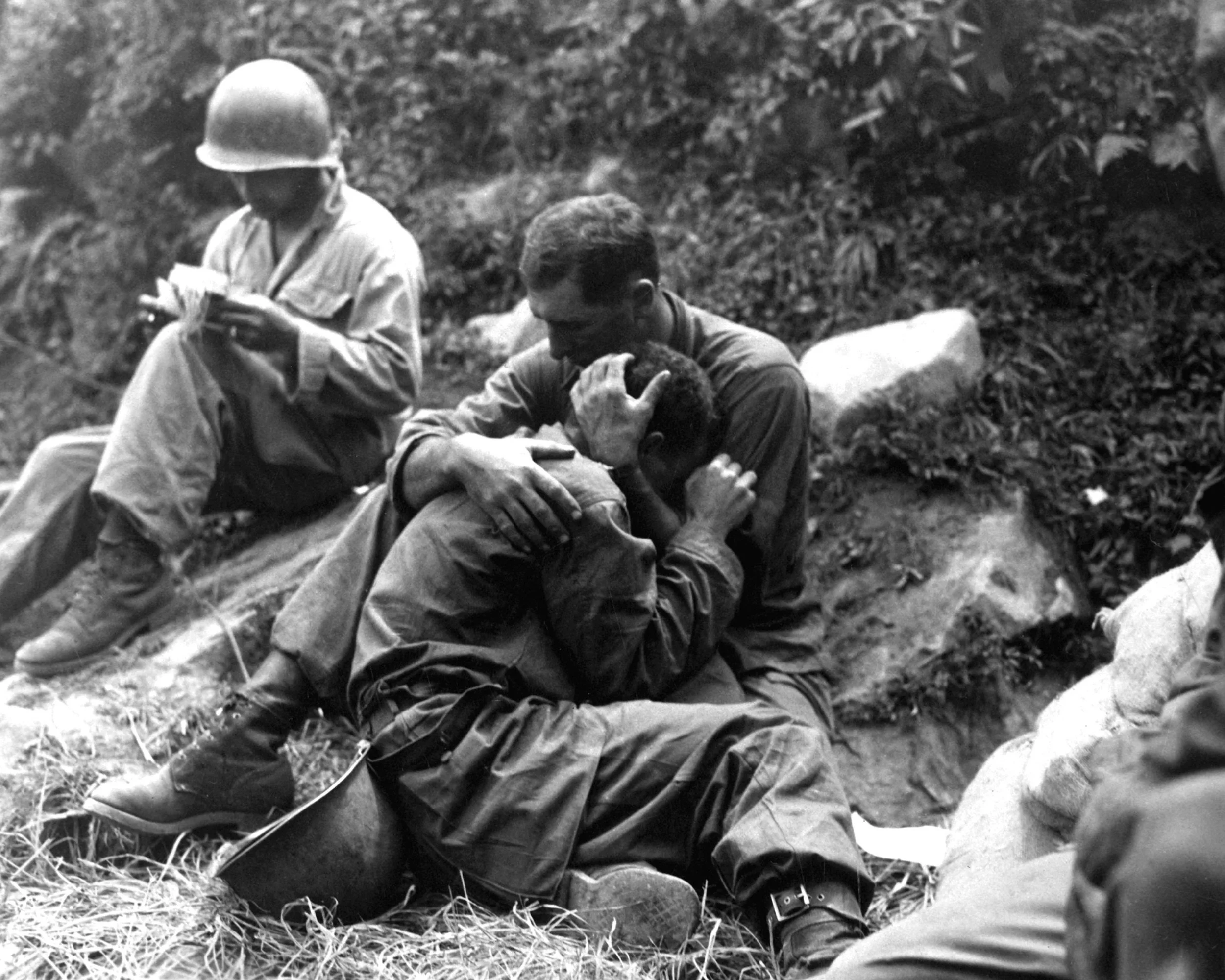 A grief stricken American infantryman whose friend has been killed in action is comforted by another soldier. In the background a corpsman methodically fills out casualty tags. Sfc. (SFC Al Chang/U.S. Army Photo)
