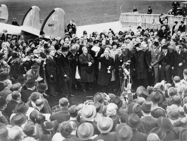 Neville Chamberlain holding the paper containing the resolution to commit to peaceful methods signed by both Hitler and himself on his return from Munich on 30 September 1938. Later that day, at 10 Downing Street, he remarked, “My good friends, for the second time in our history, a British Prime Minister has returned from Germany bringing peace with honour. I believe it is peace for our time.” (Wikimedia Commons)