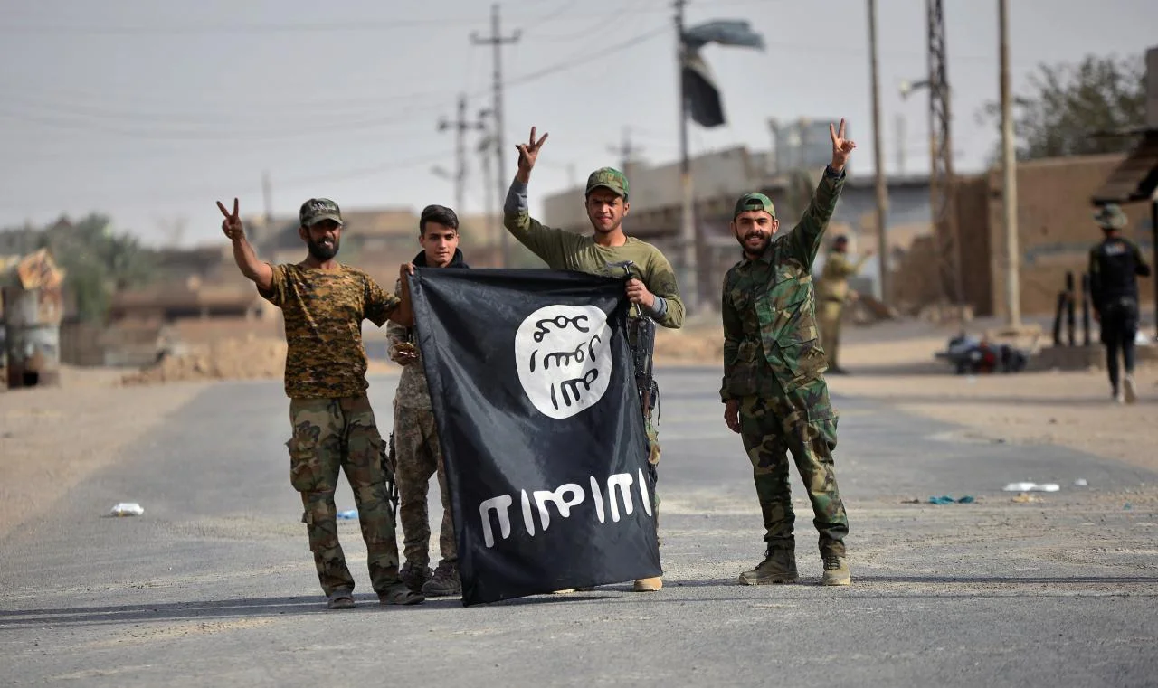 Shi’ite Popular Mobilzation Forces (PMF) fighters carry the Islamic State militants flag downward after liberating the city of Al-Qaim, Iraq November 3, 2017. (Reuters)