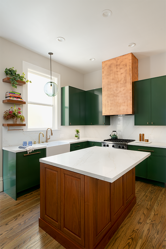 A warm walnut island anchors the emerald green kitchen, creating contrast while adding generous workspace, storage, and an inviting place to gather.
