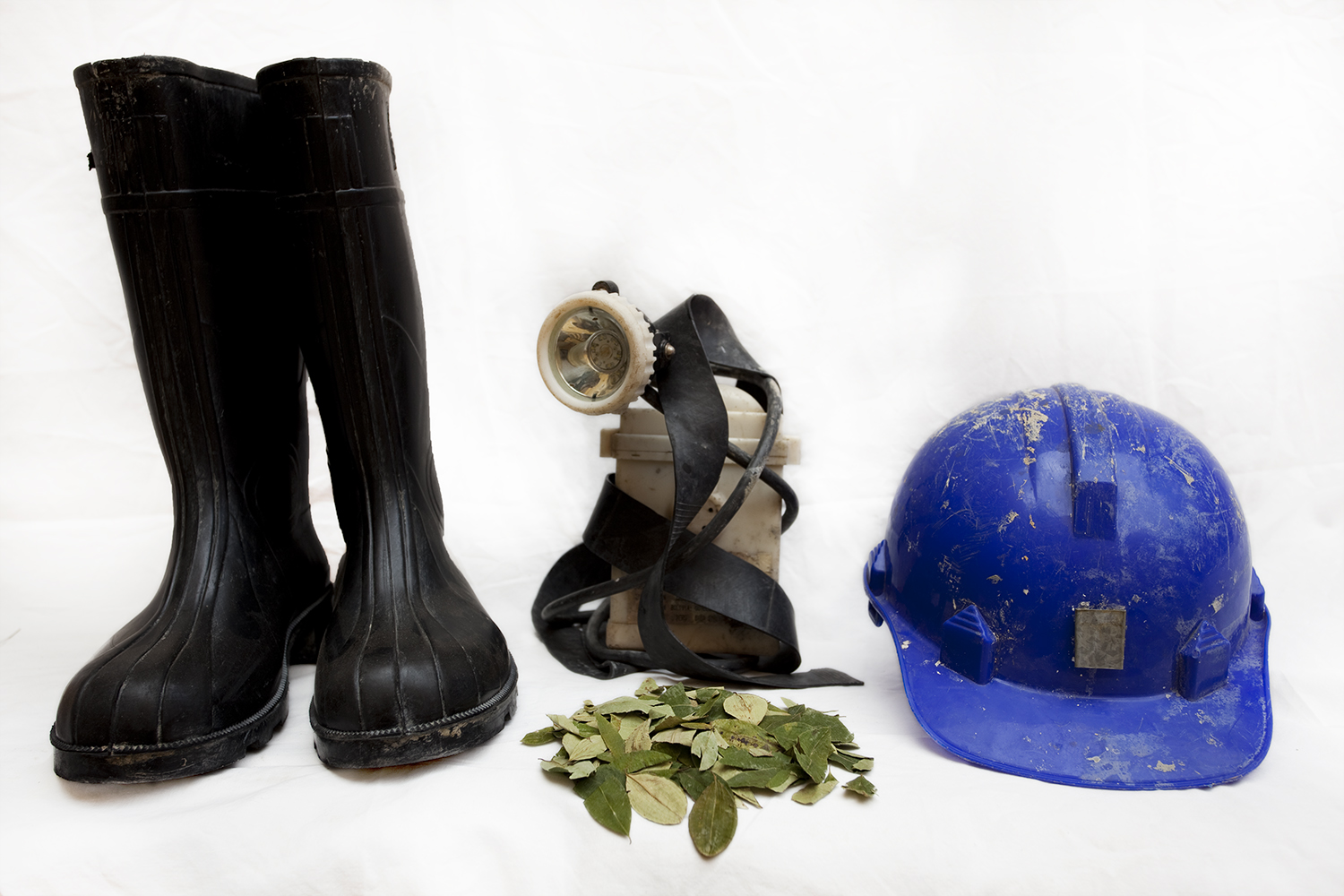  The miners' most important gear. From left, clockwise: steel-toed rain boots, a lamp, helmet, coca leaves.&nbsp; 