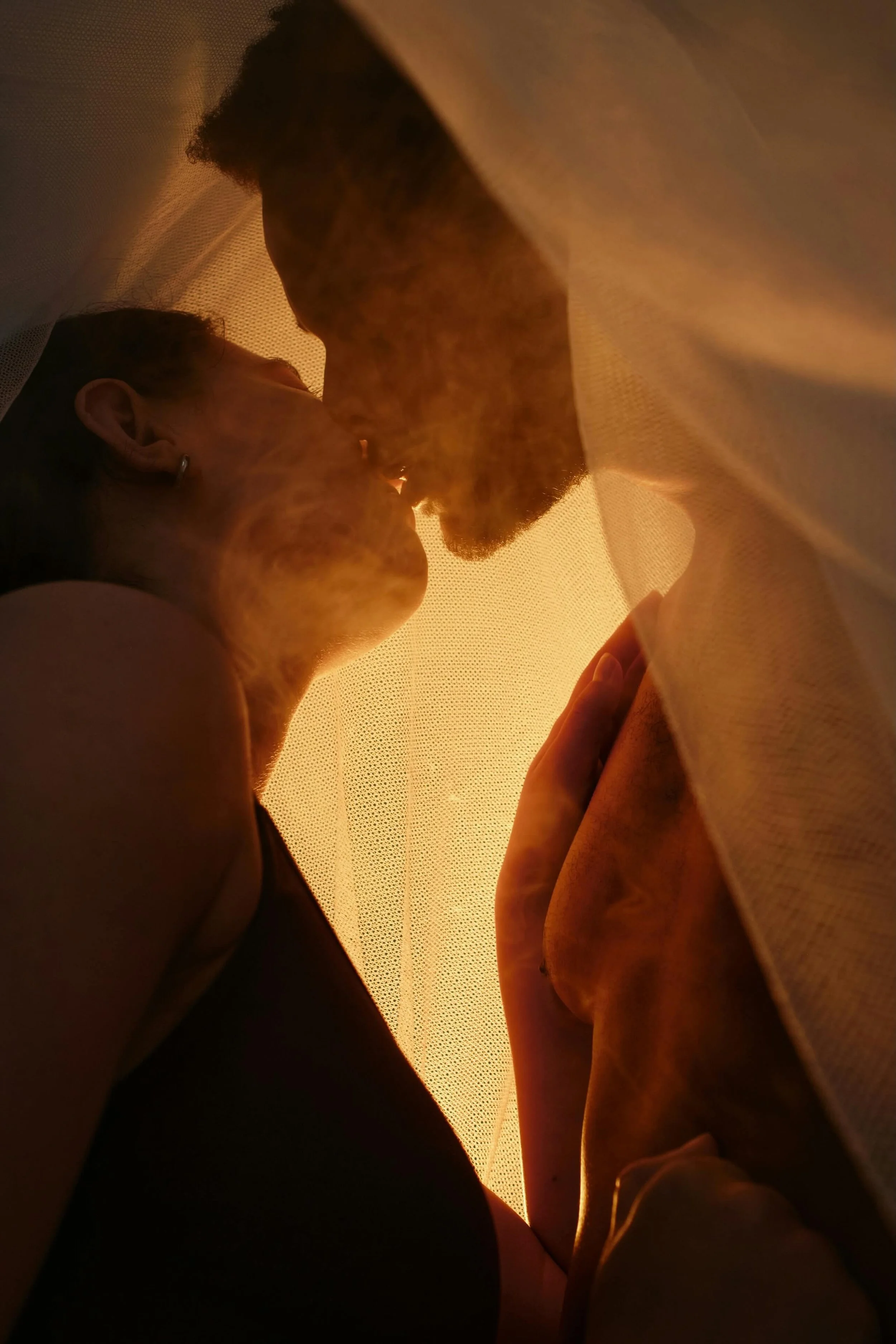 A couple with a woman and a man kissing in an intimate moment inside a softly lit space.