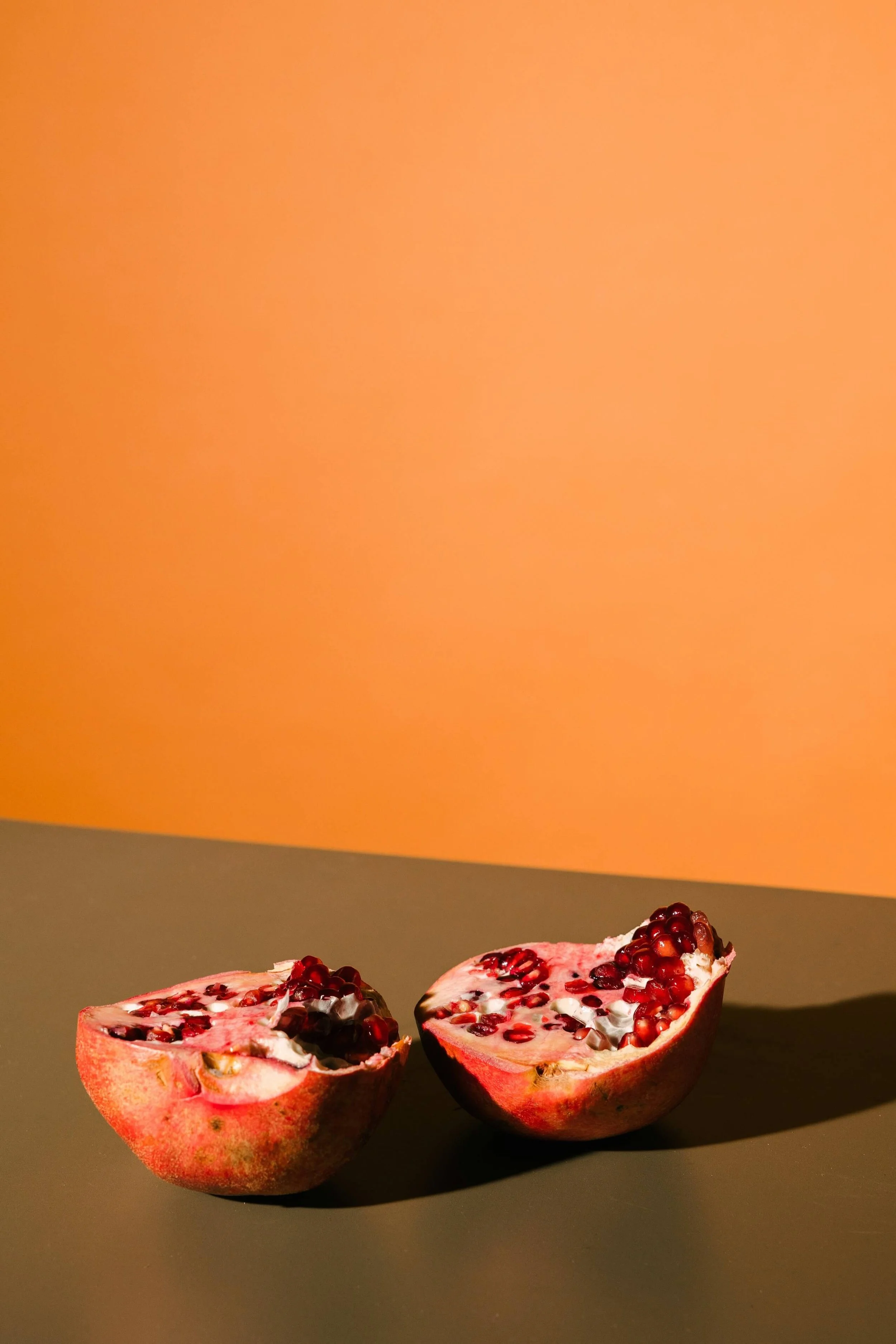 A halved pomegranate with exposed seeds on a dark surface against a plain background.