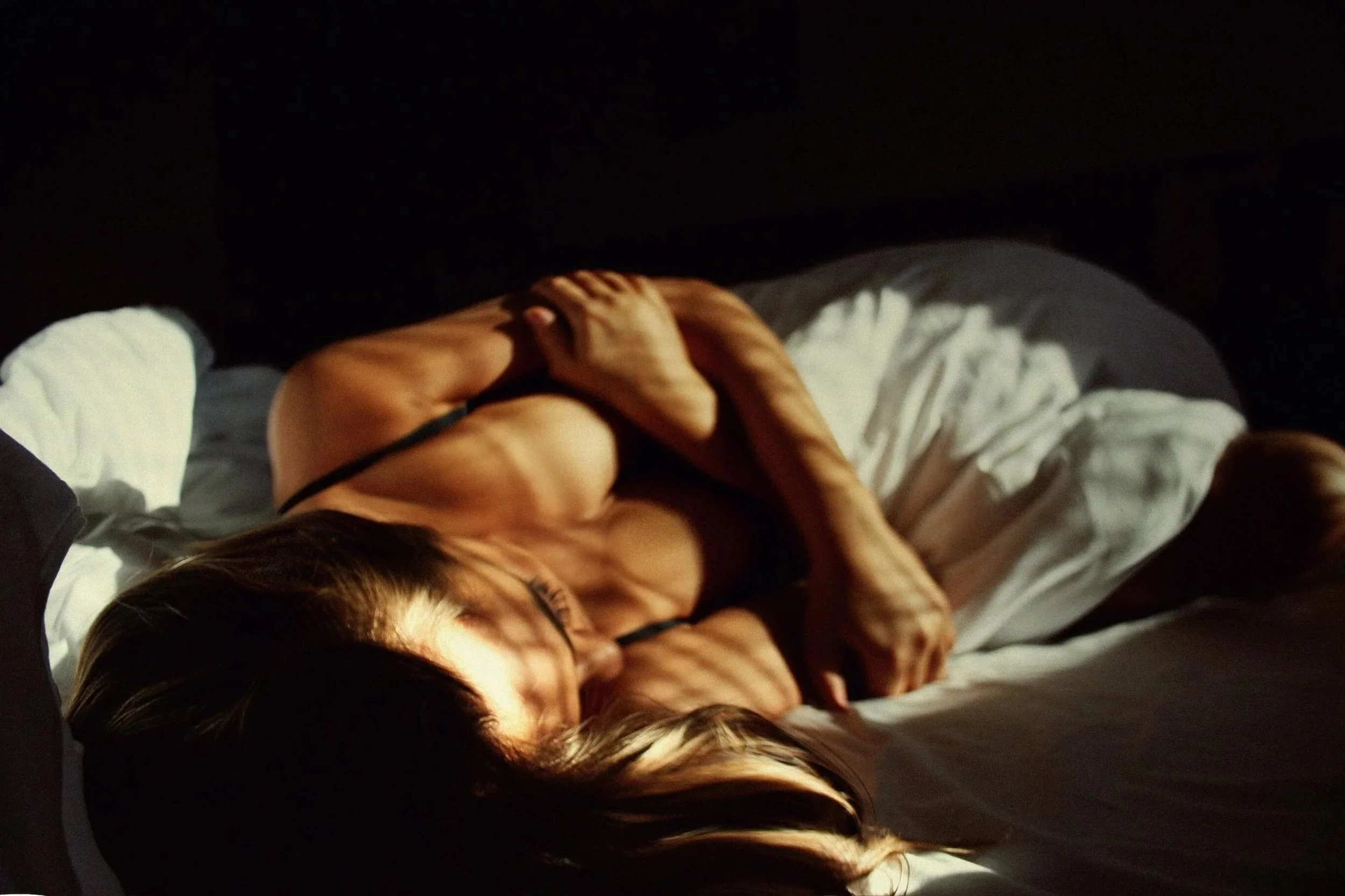 A person lying in bed with a white sheet and dark background.
