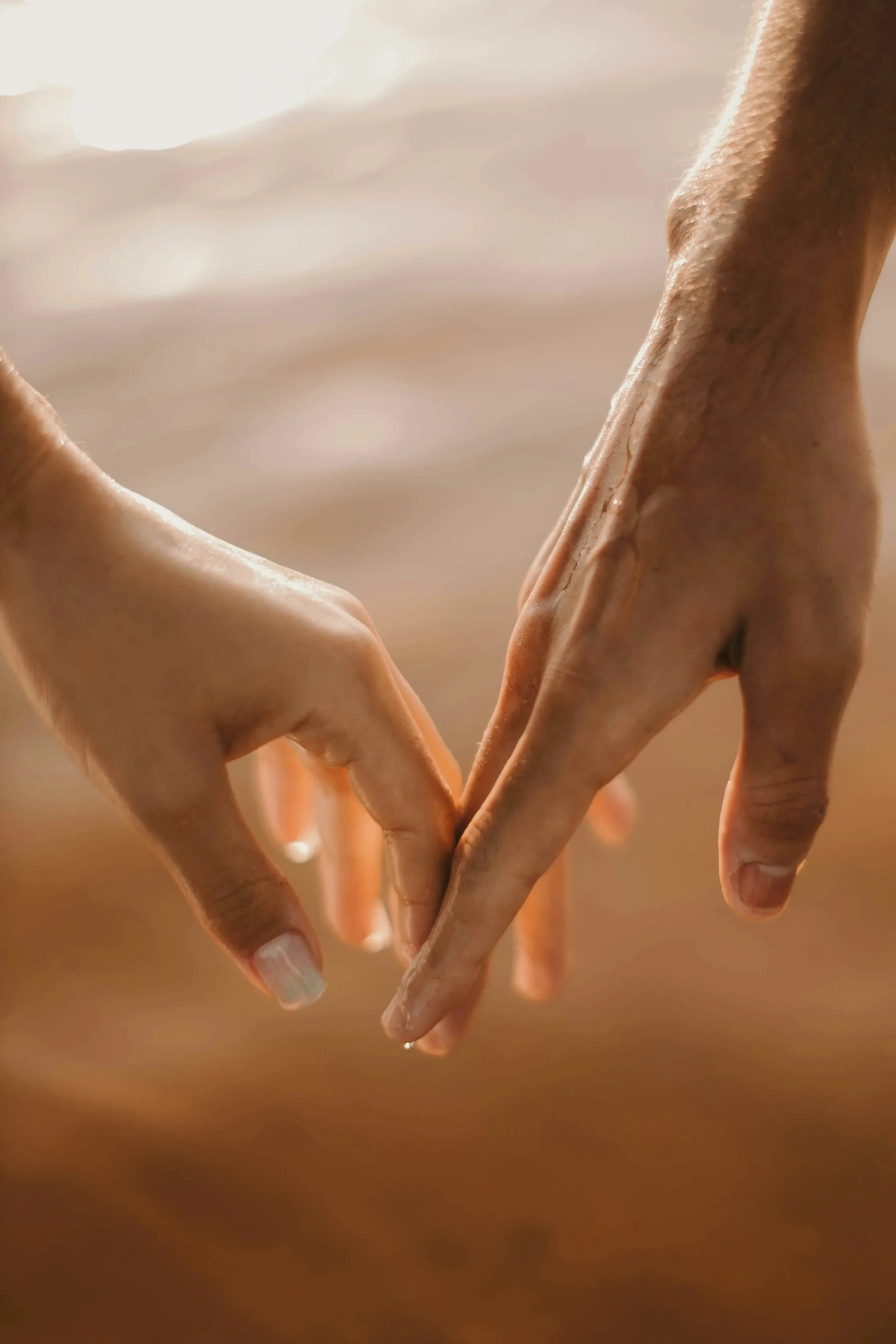 Two hands intertwined, forming a heart shape against a soft, warm background.