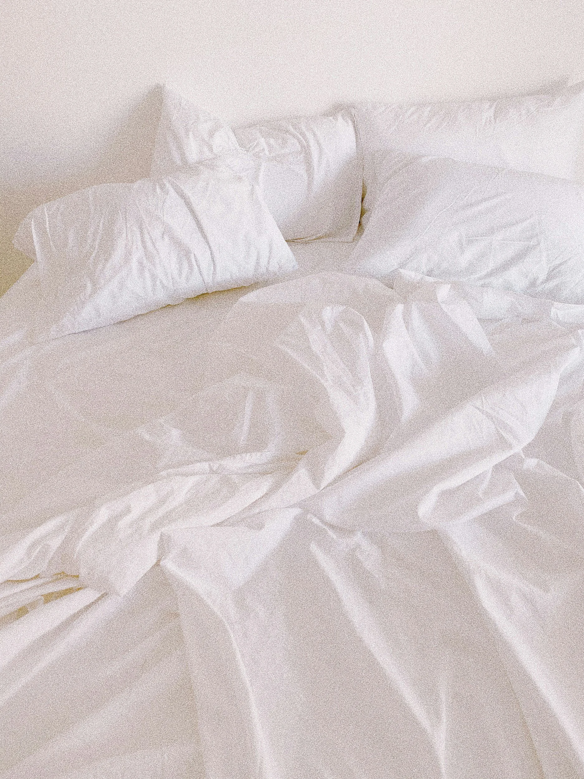 A bed with white bedsheets, pillows, and a duvet, all in a light and neutral color palette.