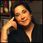 Thoughtful Indian-American woman smiles at the camera, sitting in front of book-lined shelves