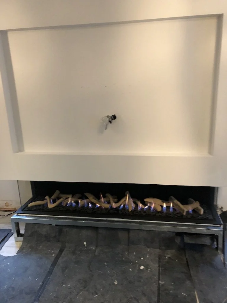 Empty built-in fireplace with a fire grate and a few small flames, a bee on the white wall inside the fireplace.