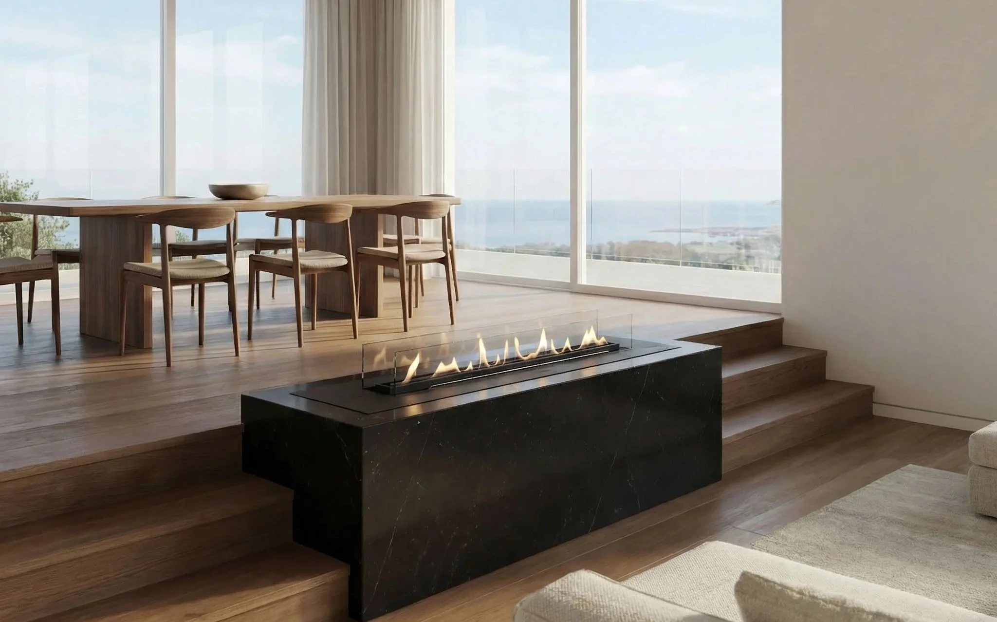Modern living room with large floor-to-ceiling windows overlooking a body of water, a dining table with wooden chairs, and a black marble fireplace with a glass barrier and flame.