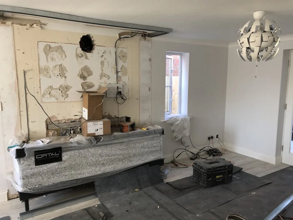 Kitchen undergoing renovation with partially demolished wall, construction tools, and materials scattered around.