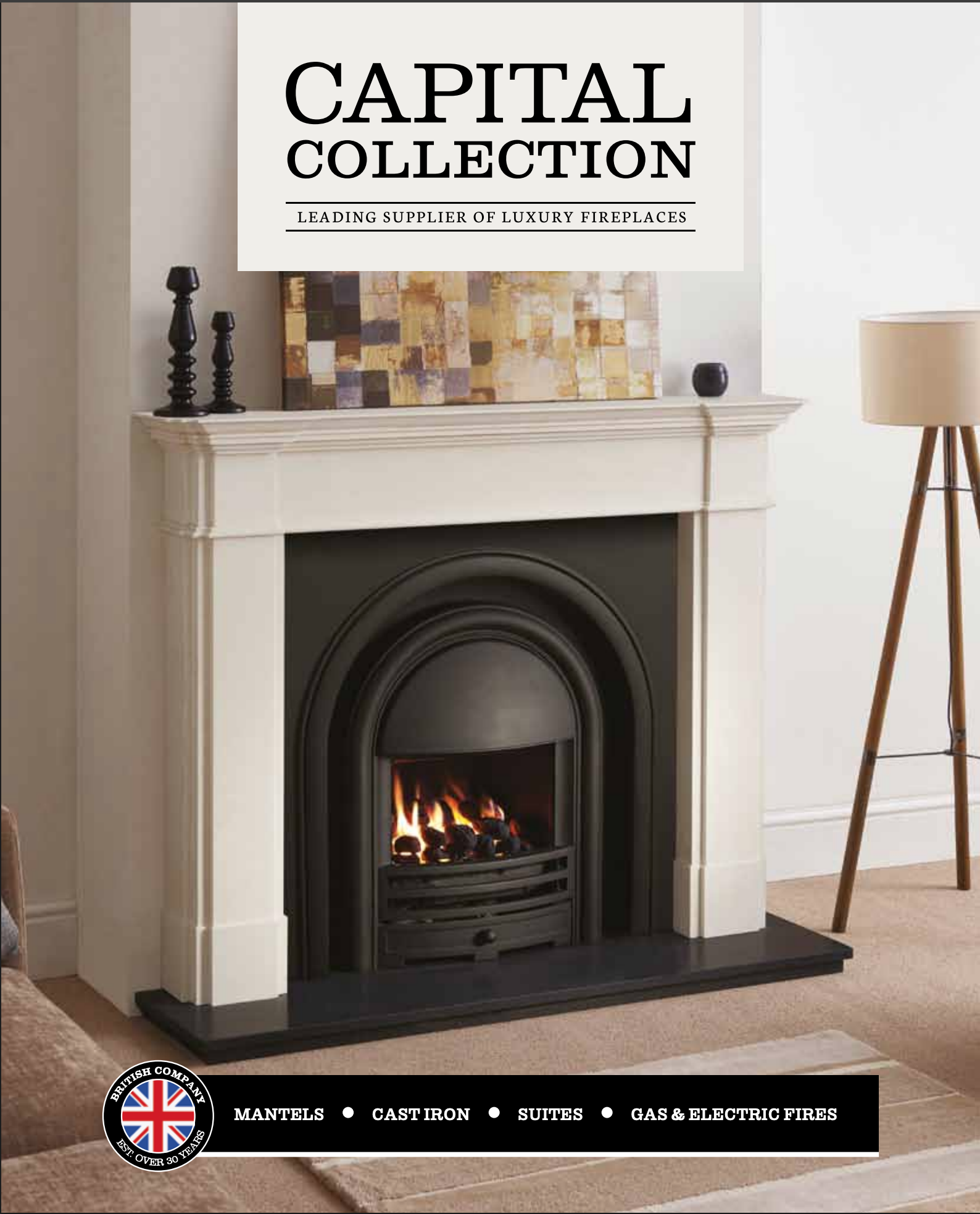 A white fireplace mantle with a black fireplace insert, above which a painting is displayed. The mantel has two black candle holders and a small black vase. To the right of the fireplace, there is a wooden tripod floor lamp with a white lampshade. A beige carpet and a tan rug are visible on the floor in front of the fireplace. The bottom part of the image features a black banner with a British flag logo and text that reads: "Mantels, Cast Iron, Suites, Gas & Electric Fires, Est. Over 30 years."