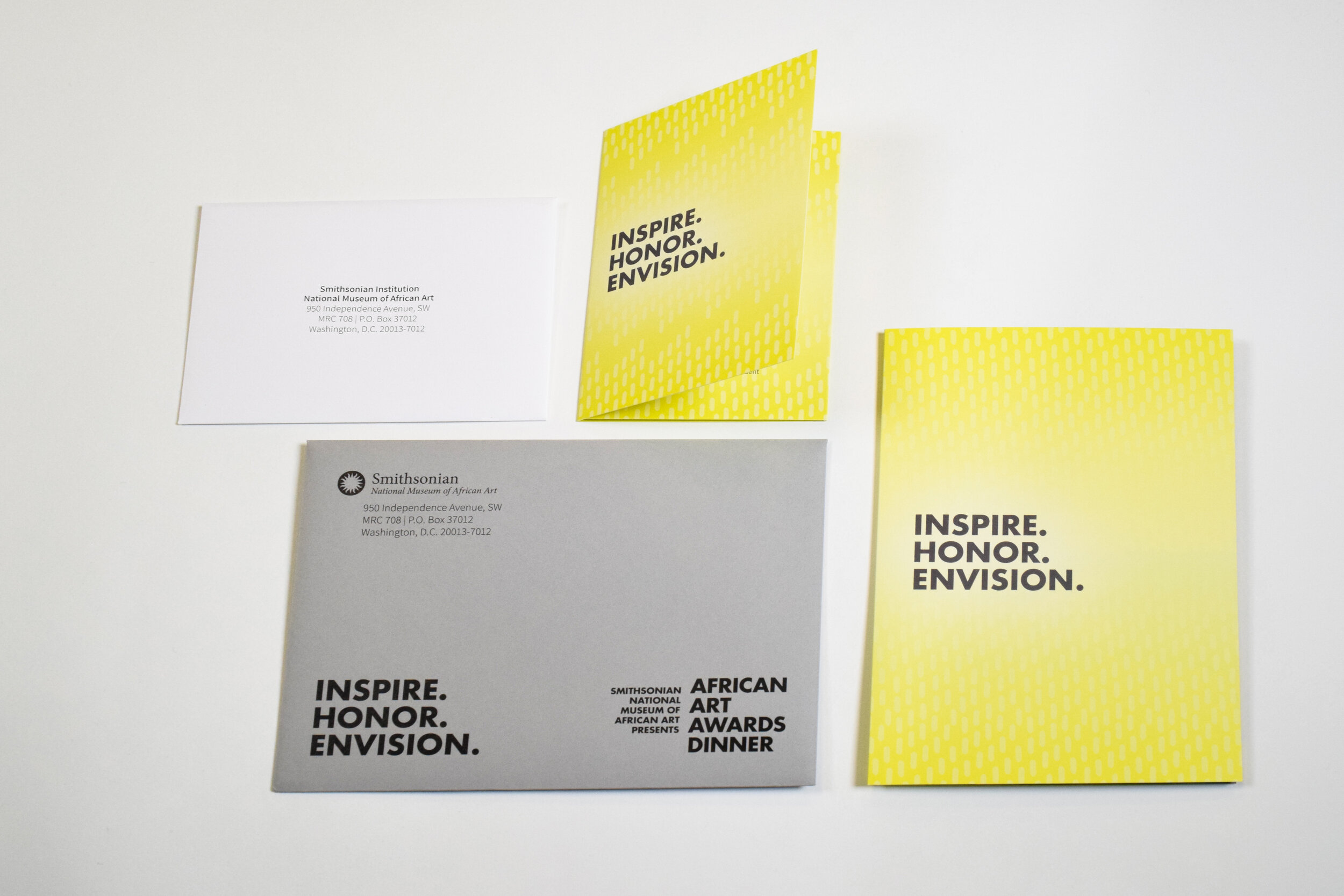 A suite of printed inviation collateral including a yellow invitation and RSVP card with gray and white envelopes.