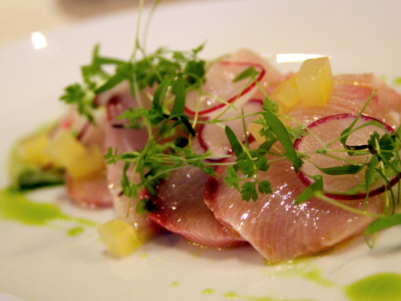  Crane Bay® Katsu Hamachi Crudo served with a scattering of pea vines and sliced radishes with chunks of daikon, stone fruit and avocado