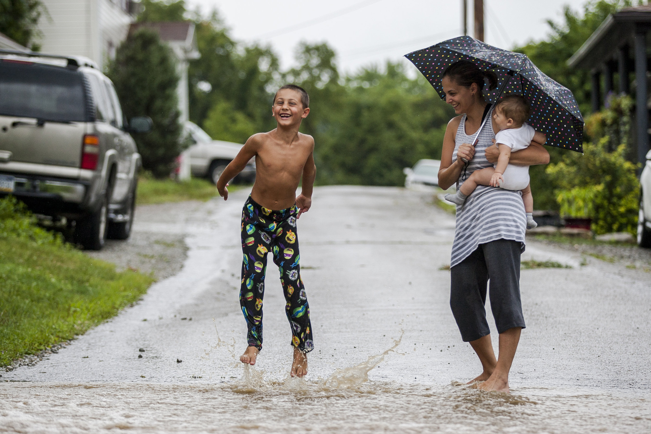 Robert Repovz, 6, splashes through rain water running across First Street while his mother Anita and baby sister Gabriella watch in New Stanton, Pennsylvania, on Saturday, July 30, 2016.
