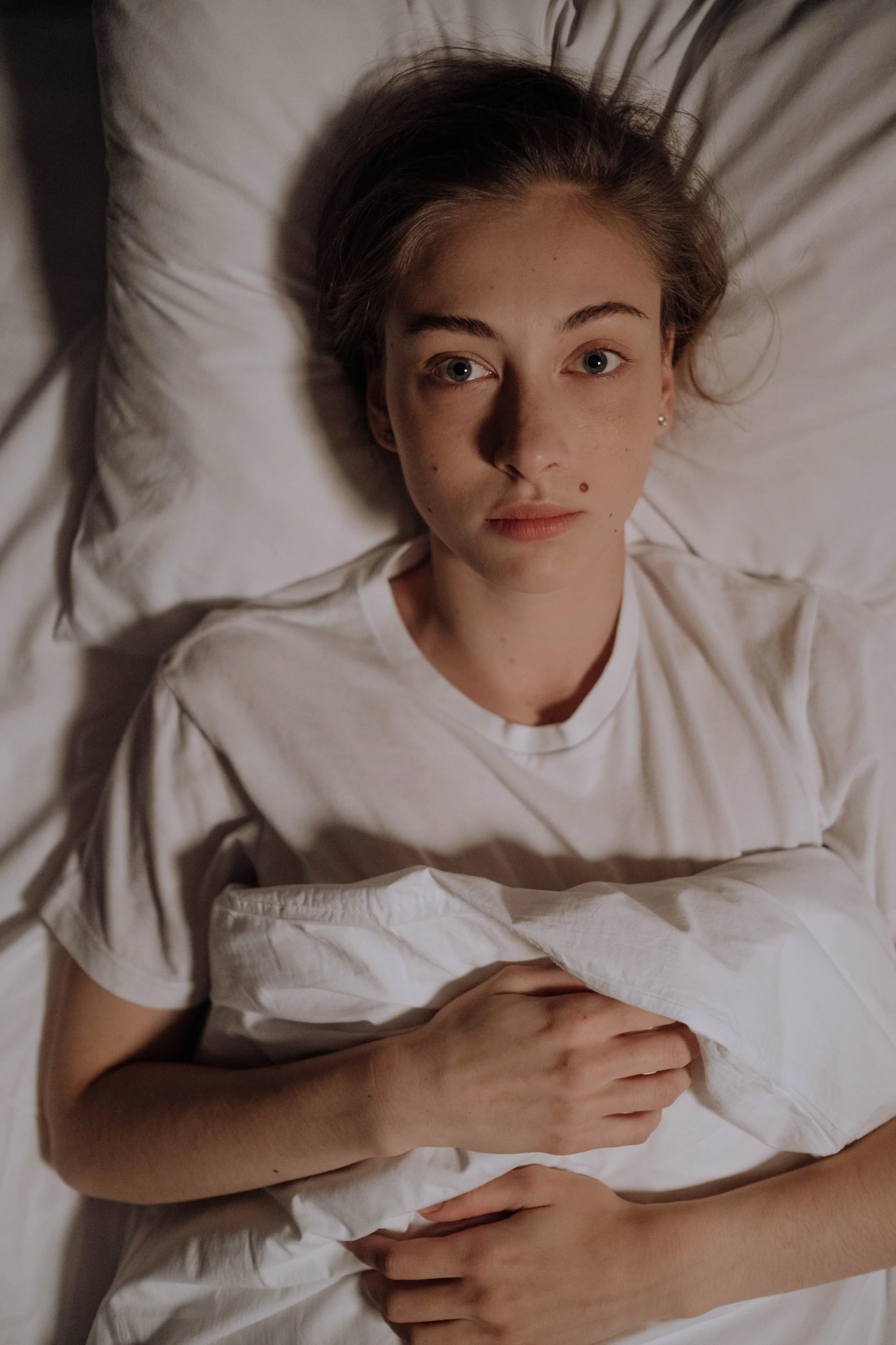 An mage of a female person lying in bed, thinking of frustrating things instead of sleeping.