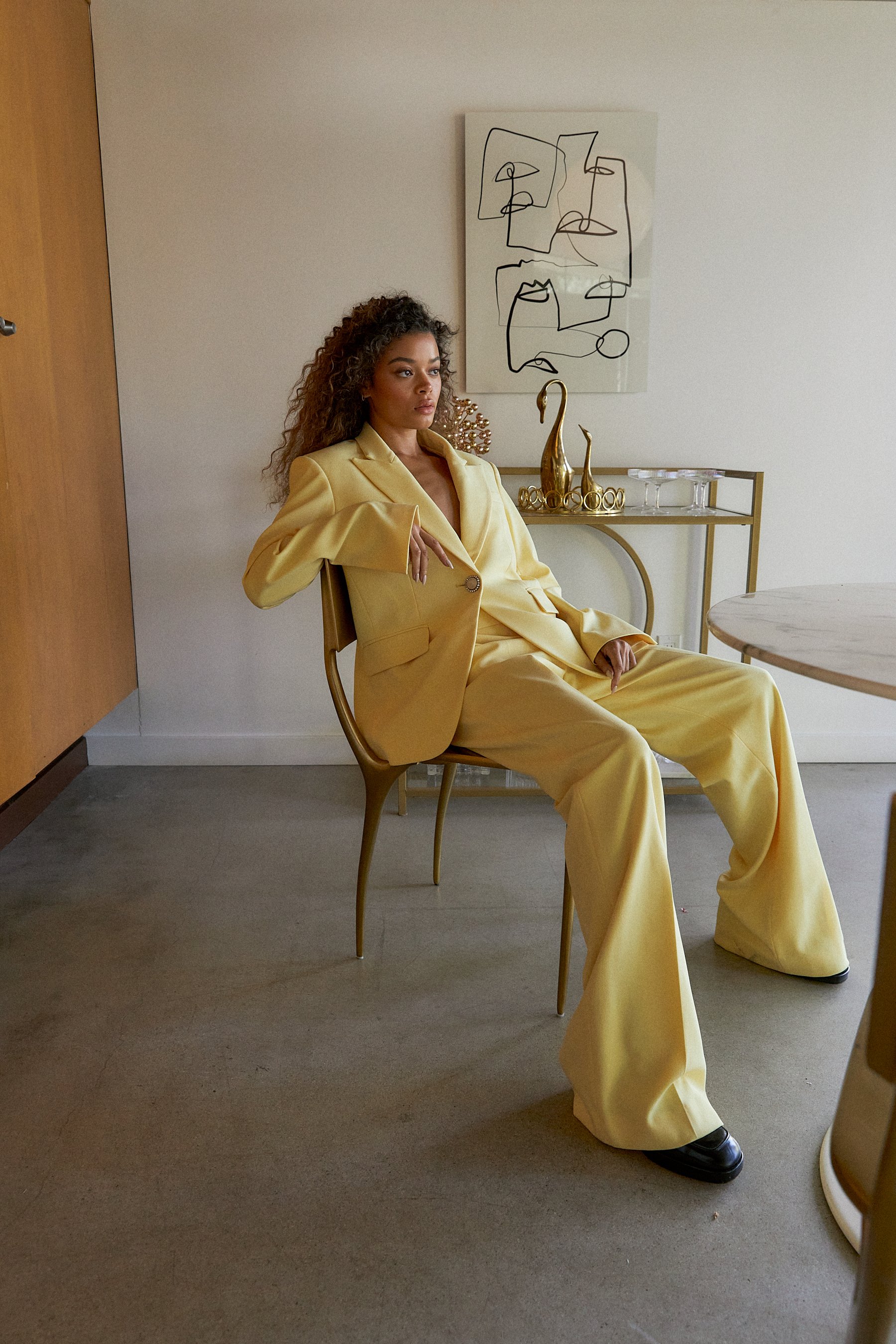  Model shot in pastel yellow suit seated at table. Styled by Emily Burnette. 