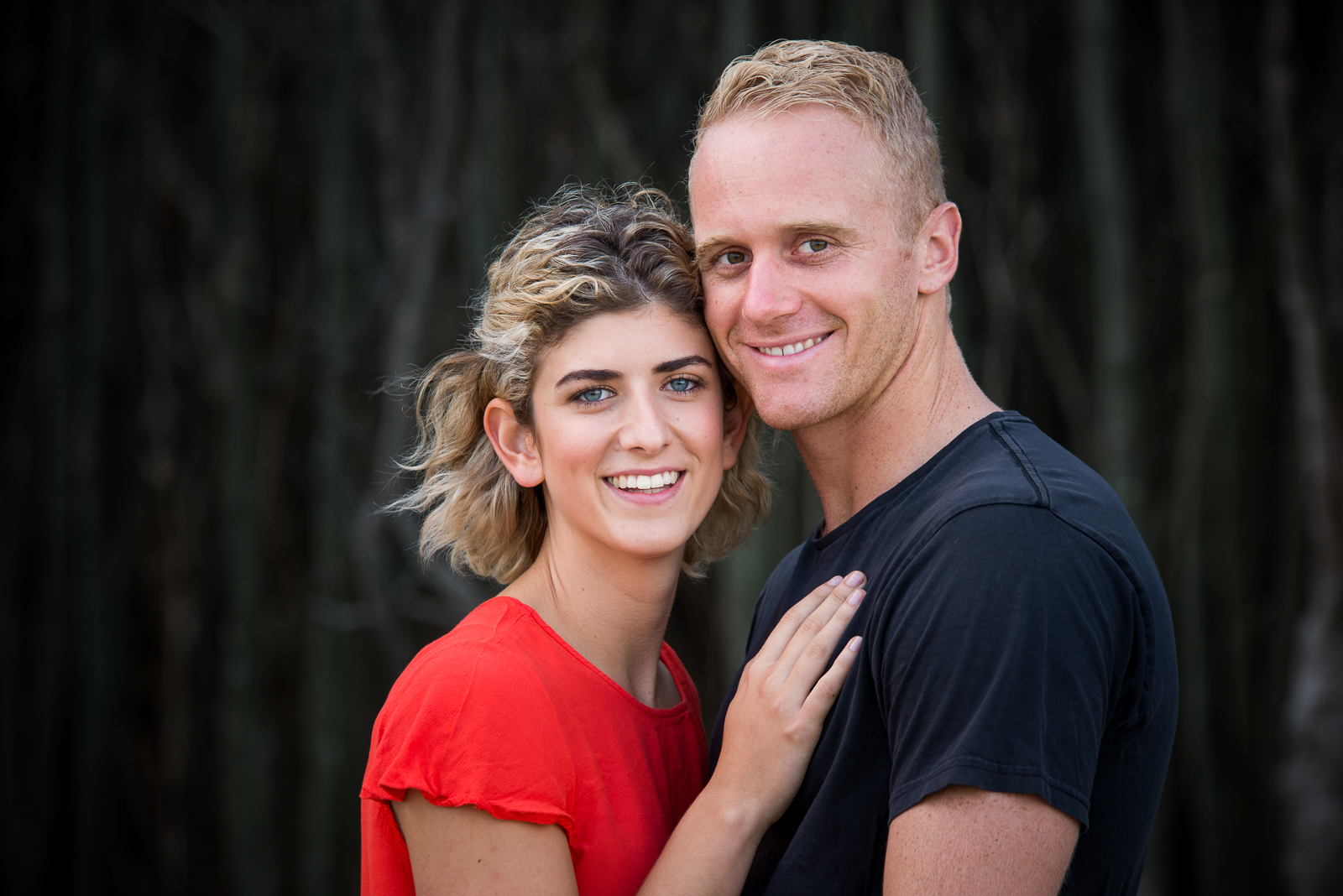 Engaged couple against dark tree background