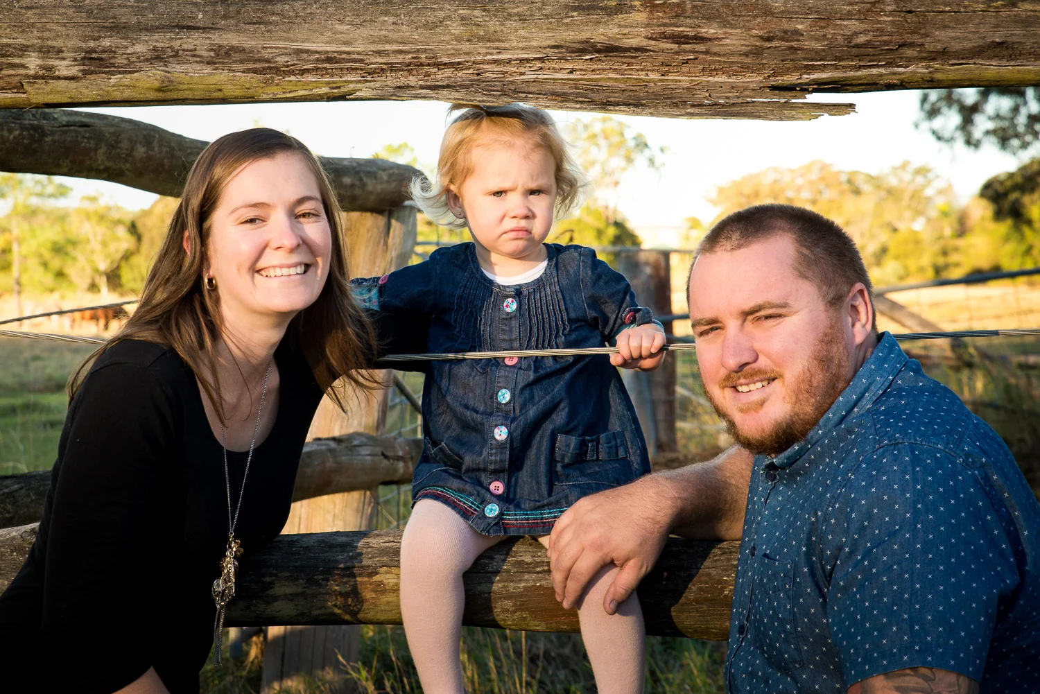 Mum dad and daughter in cattle fence warm afternoon sunlight