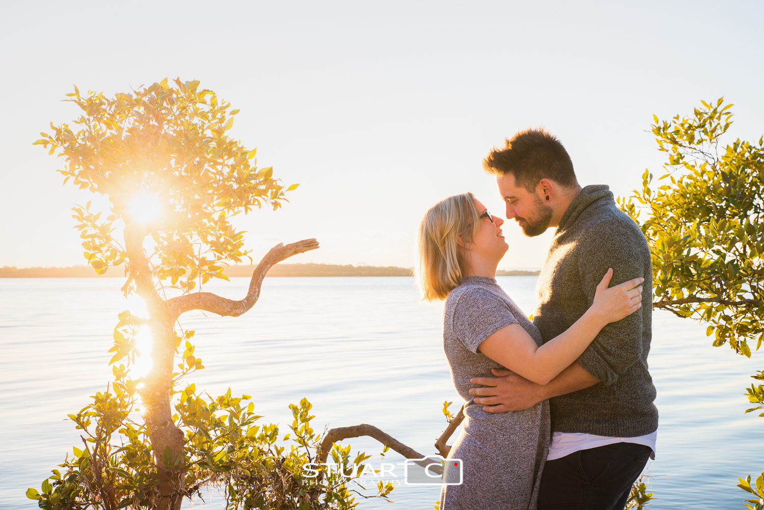 engaged couple between trees backlit at beach
