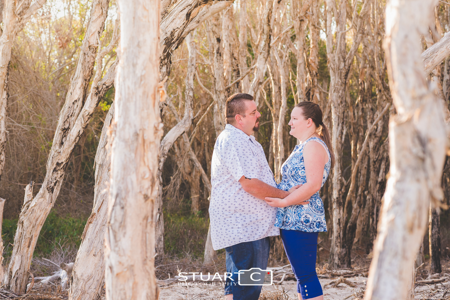 engaged couple wearing white and blue in amongst paper bark trees at beach