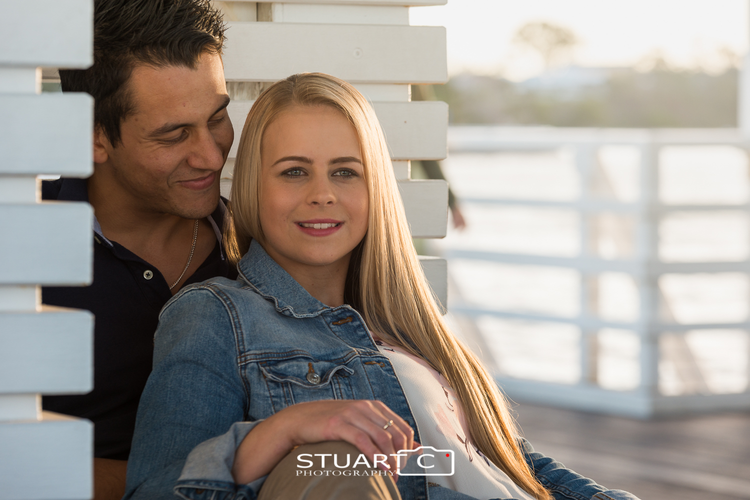 engaged couple sitting on pier at sunset
