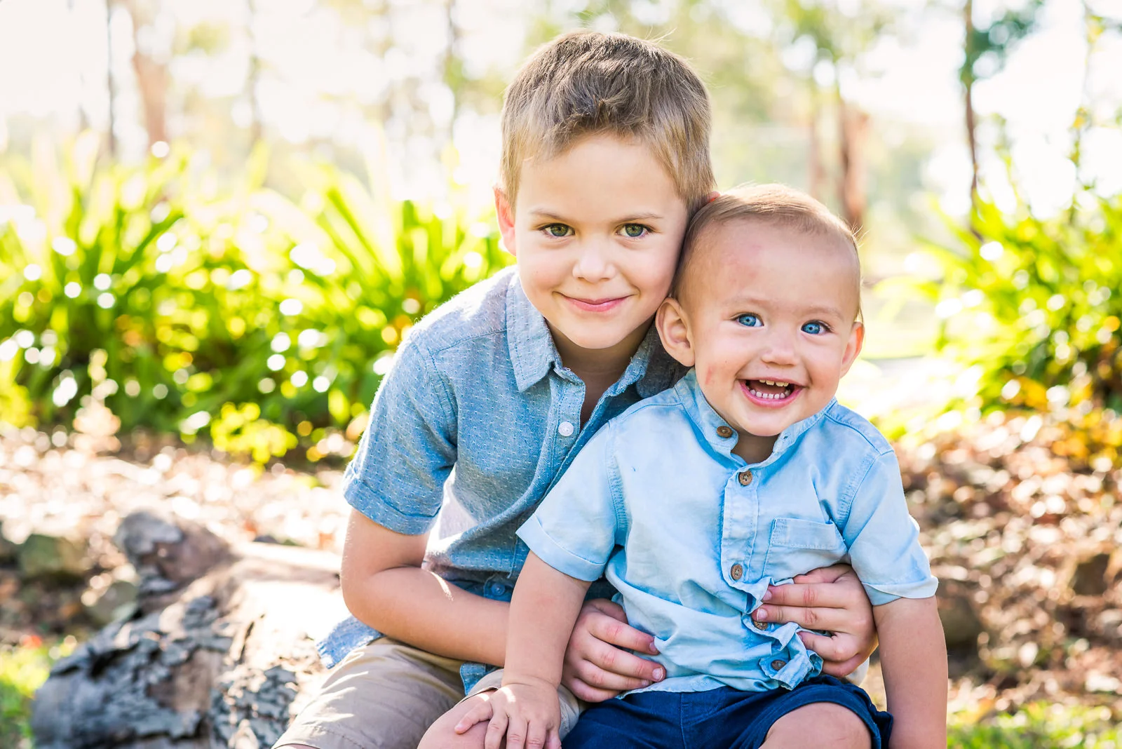 Family portrait of young children brothers sitting on a log laughing in garden setting at home in Caboolture
