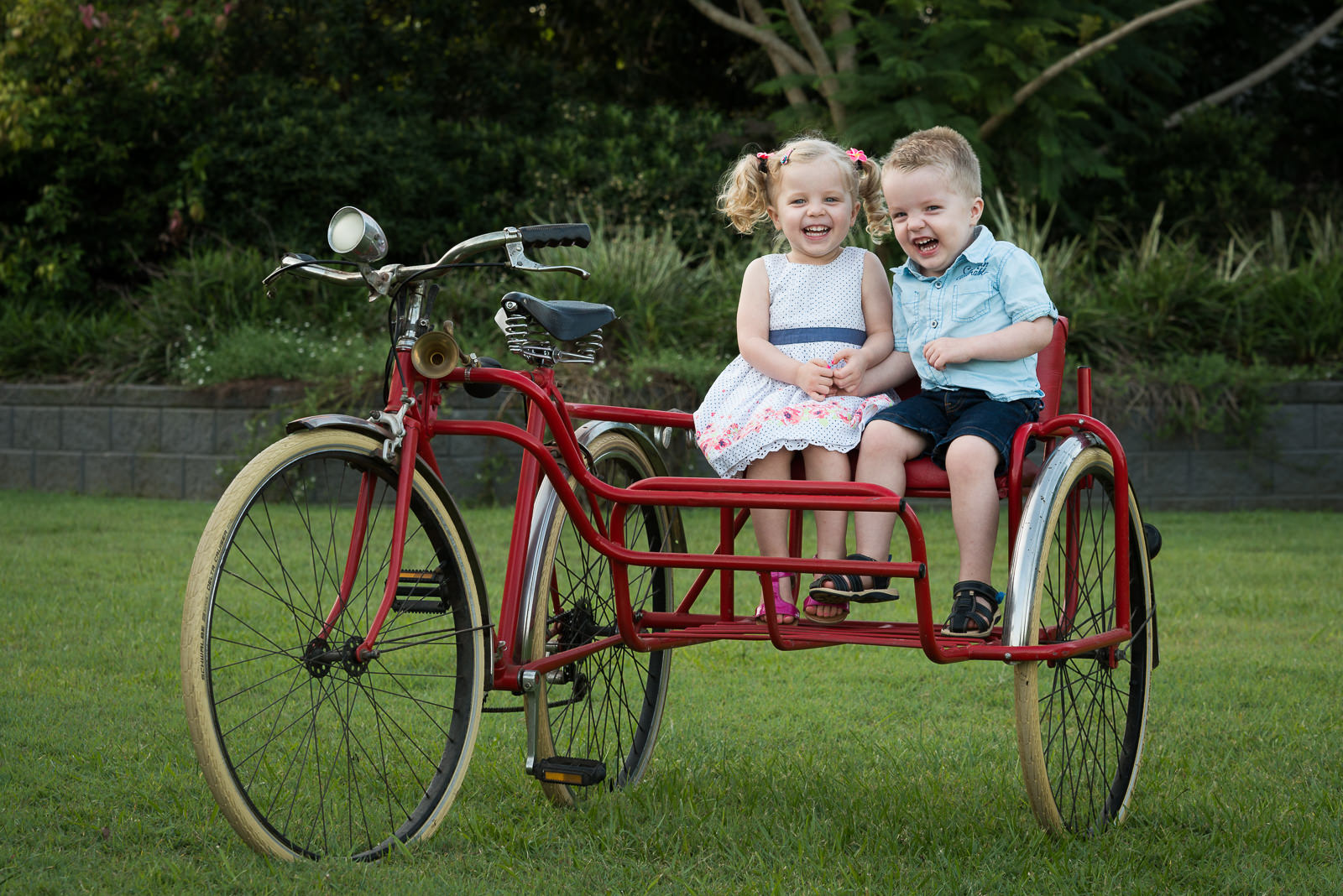 portrait of twin brother and sister sitting on vintage bike at home in the garden, elimbah