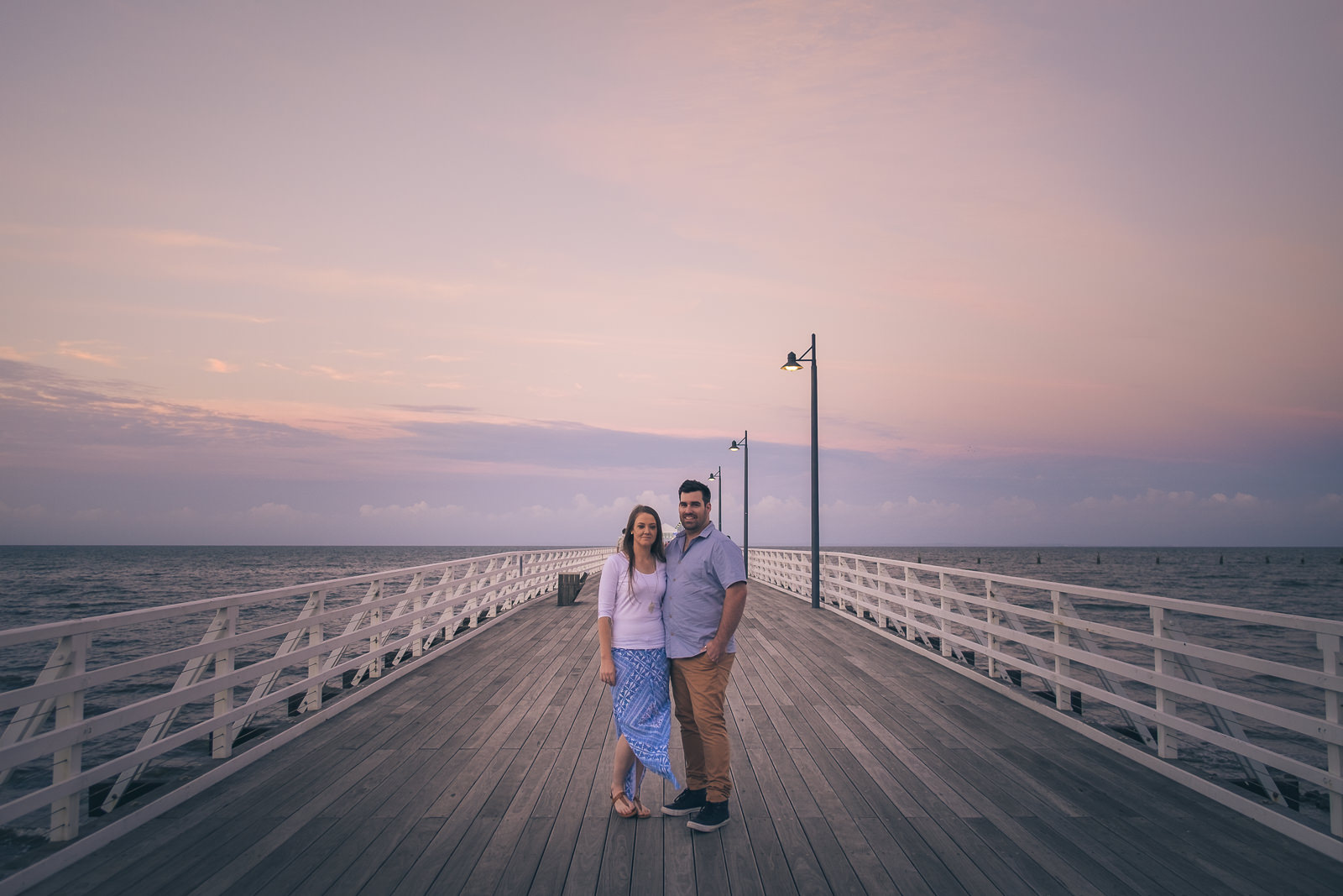 engaged couple standing on shorncliffe pier at sunset