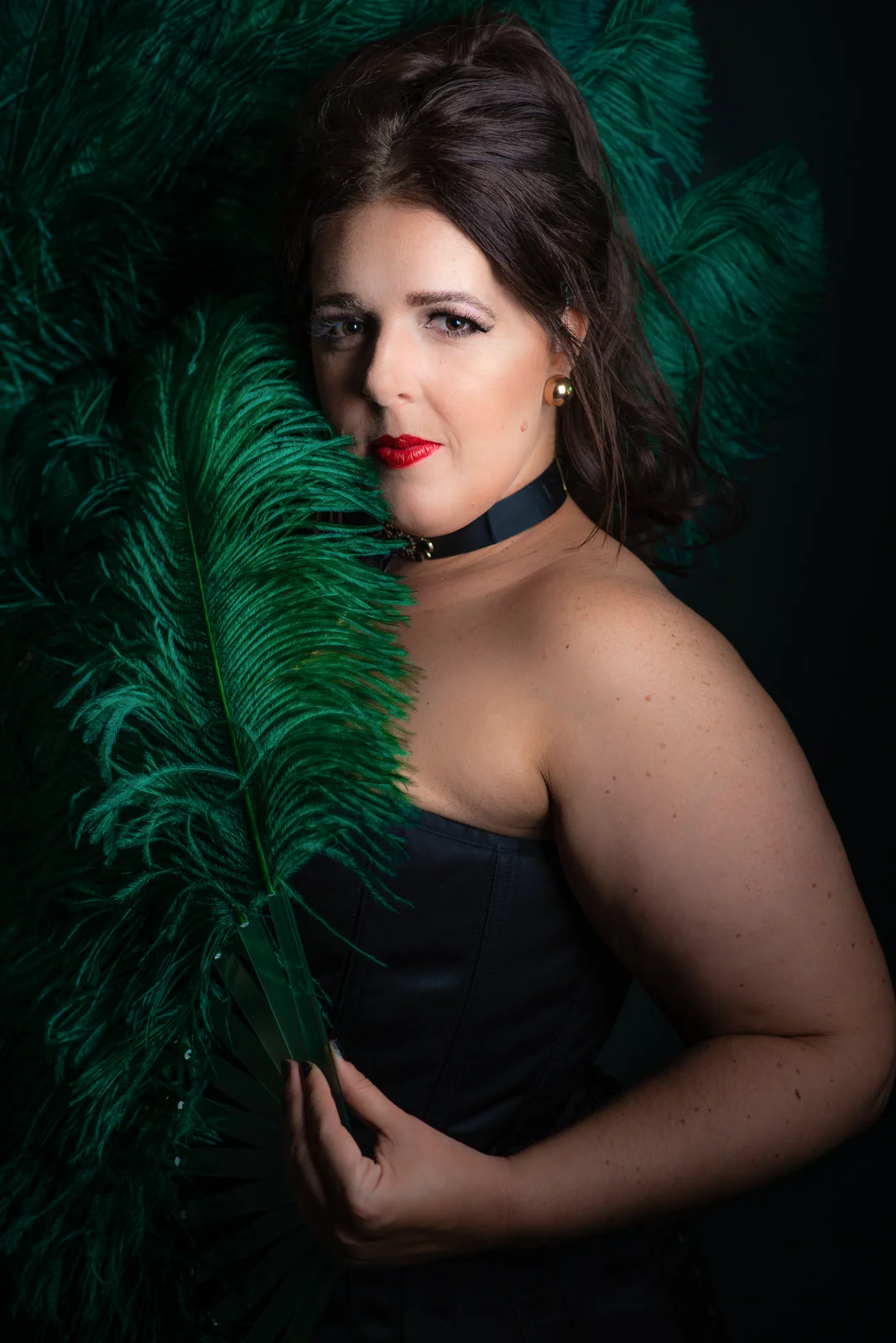Up close portrait of Cora Confetti burlesque performer wearing black corset and holding green feather fans. Caboolture portrait photography