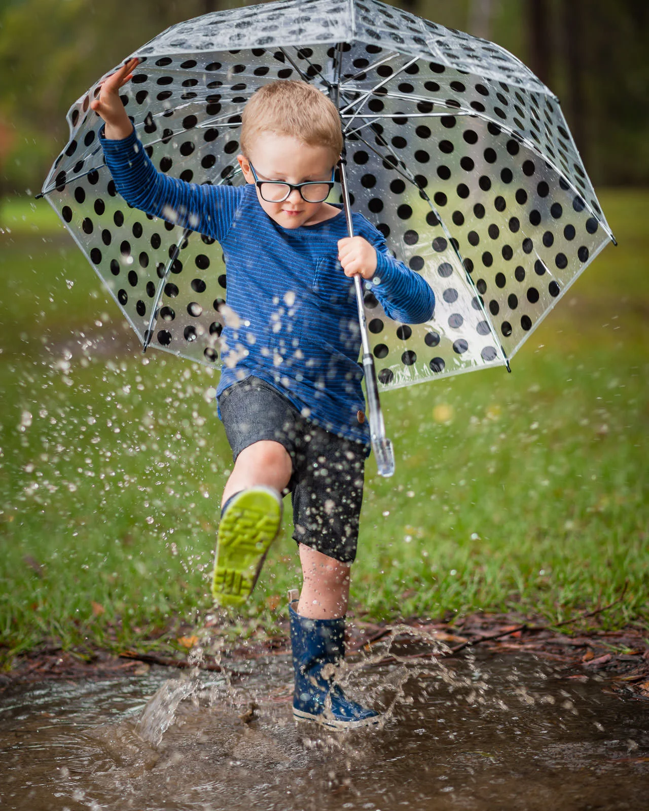 Young boy splashing in puddles in the park with a big clear umbrella as it rains | caboolture outdoor family photographer