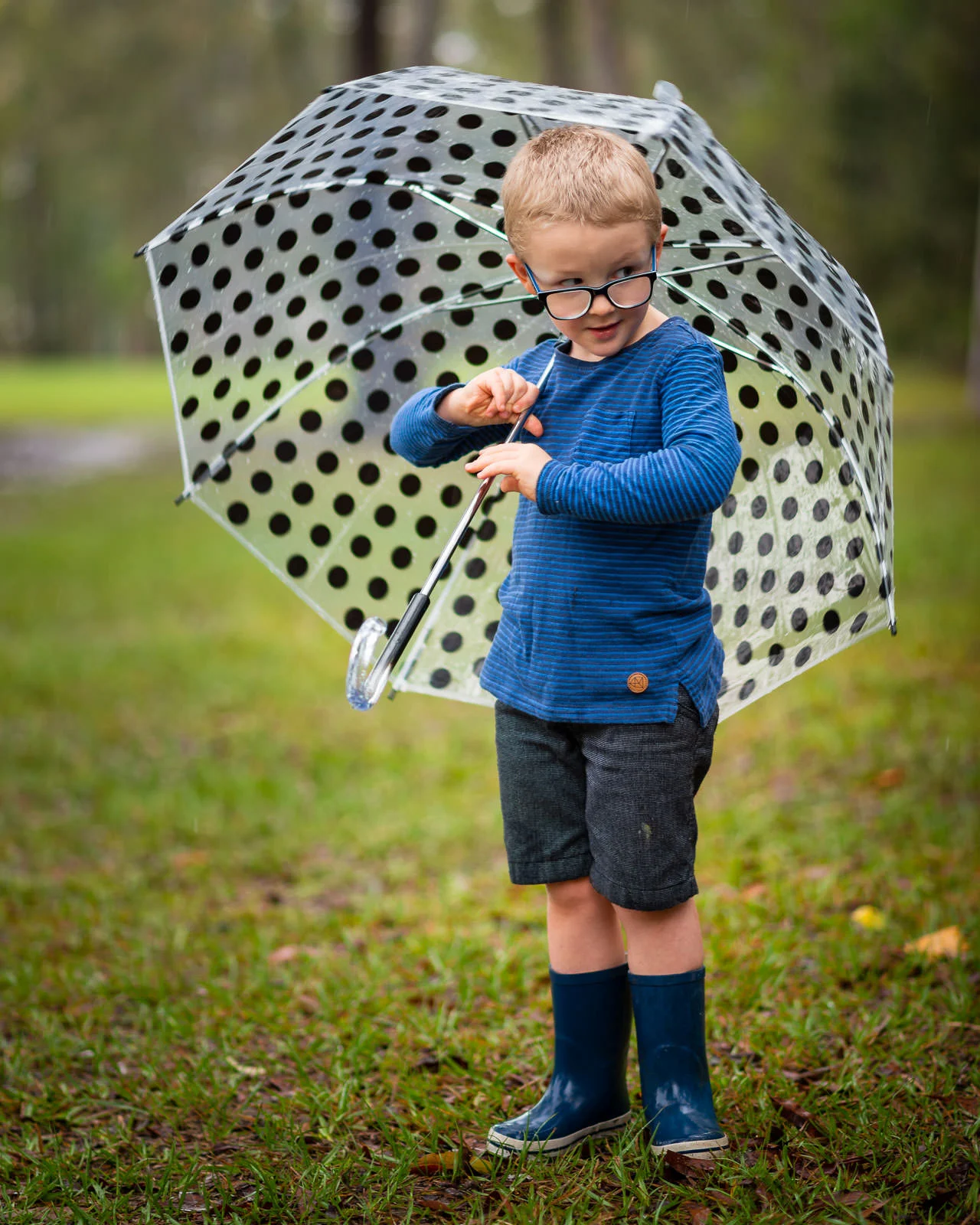 Portrait of child wearing gumboots and holding an umbrella as it rains in a caboolture park | North Brisbane family portrait photographer