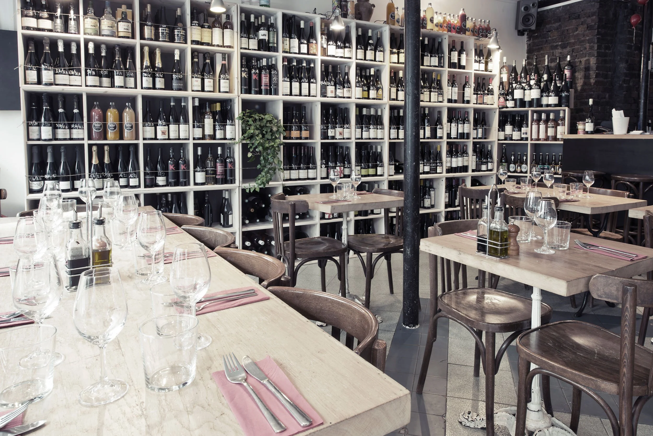 Restaurant  du Ballon Rouge à Paris, avec des tables en bois, des verres à vin, des bouteilles d'huile, et un mur avec des étagères remplies de bouteilles de vin.
