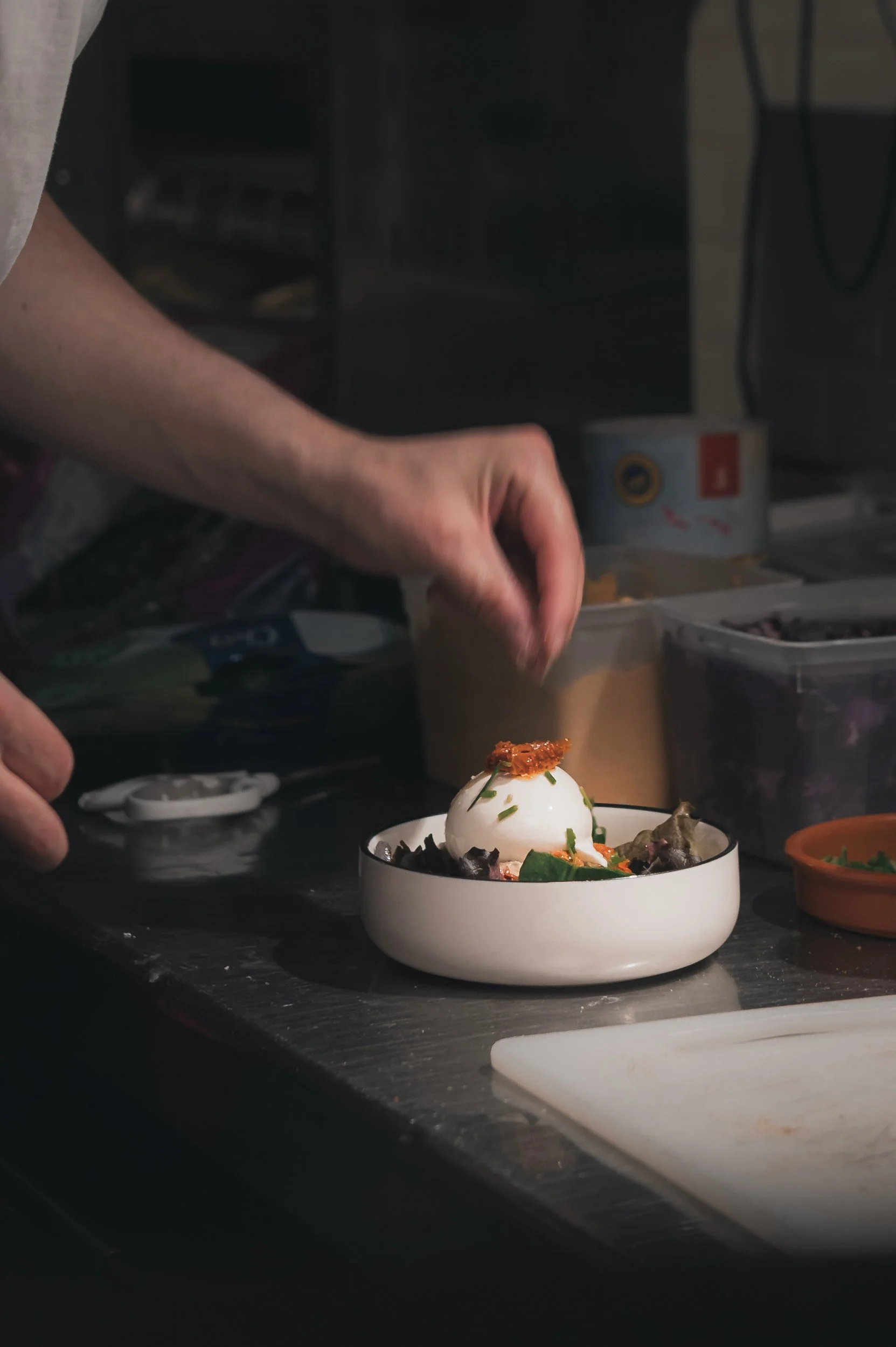 Restaurant Le Ballon Rouge, Personne ajoutant de la sauce ou de la garniture sur un plat avec une boule de mozzarella, dans une cuisine.