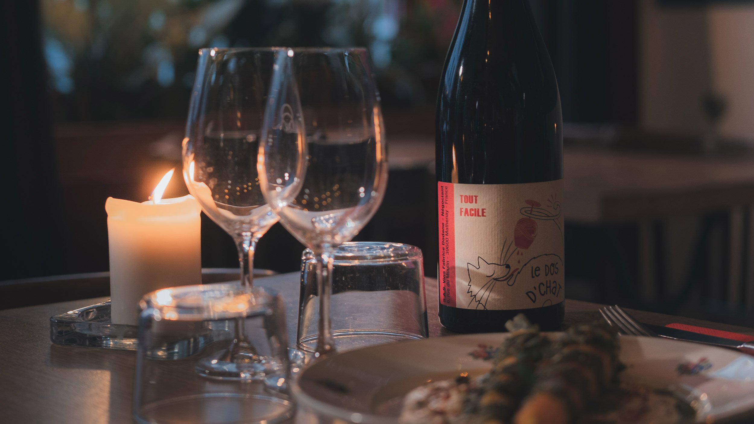 Restaurant Le Ballon Rouge, Verre à vin vide, bouteille de vin avec étiquette, bougie allumée, assiette avec nourriture, et plusieurs autres verres sur une table lors d'un dîner.