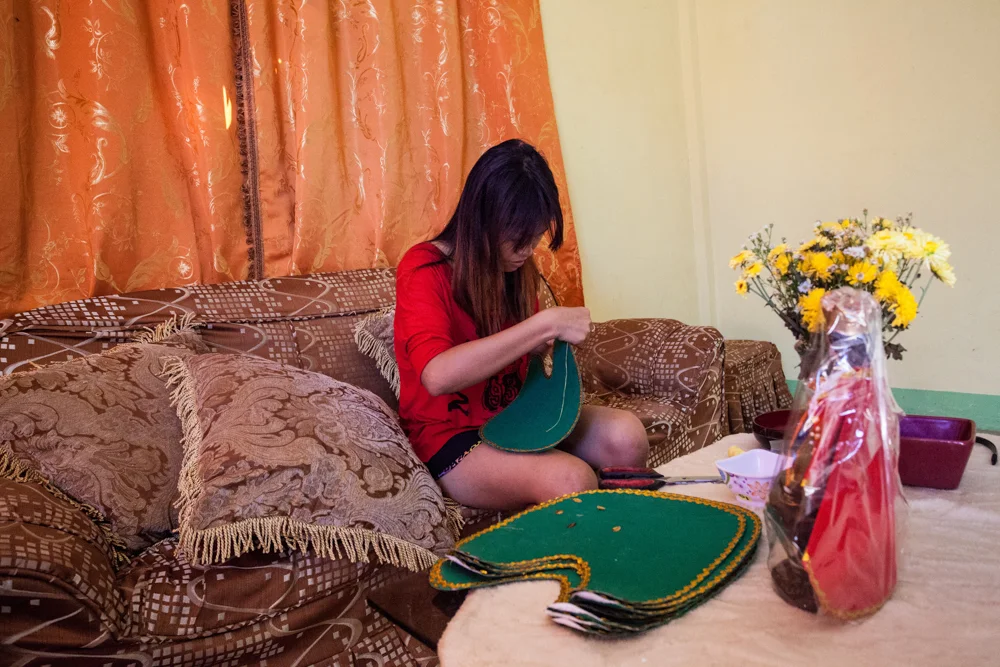 Divine Astorga, 22,&nbsp;sews clothes that will accompany religious figurines. In addition to selling popsicles and working in their small storefront, the sisters sell the figurines at upcoming festivals to earn money for their commute in and out of