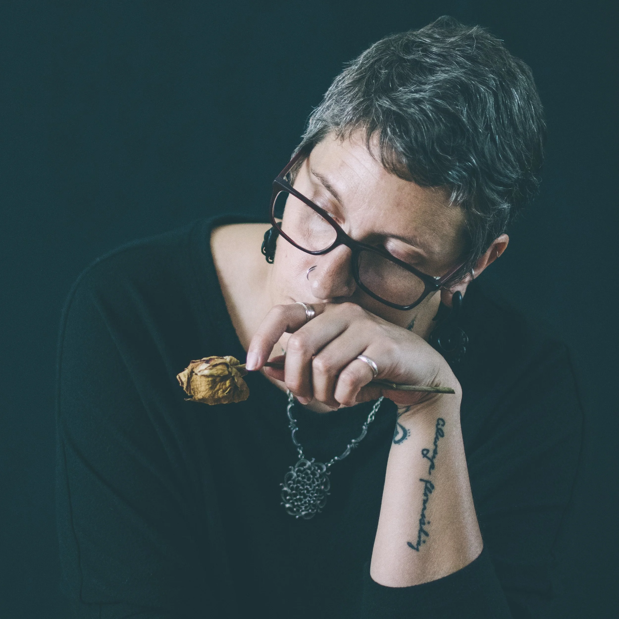 A slightly desaturated image of a woman with short hair and glasses holding a dried yellow rose