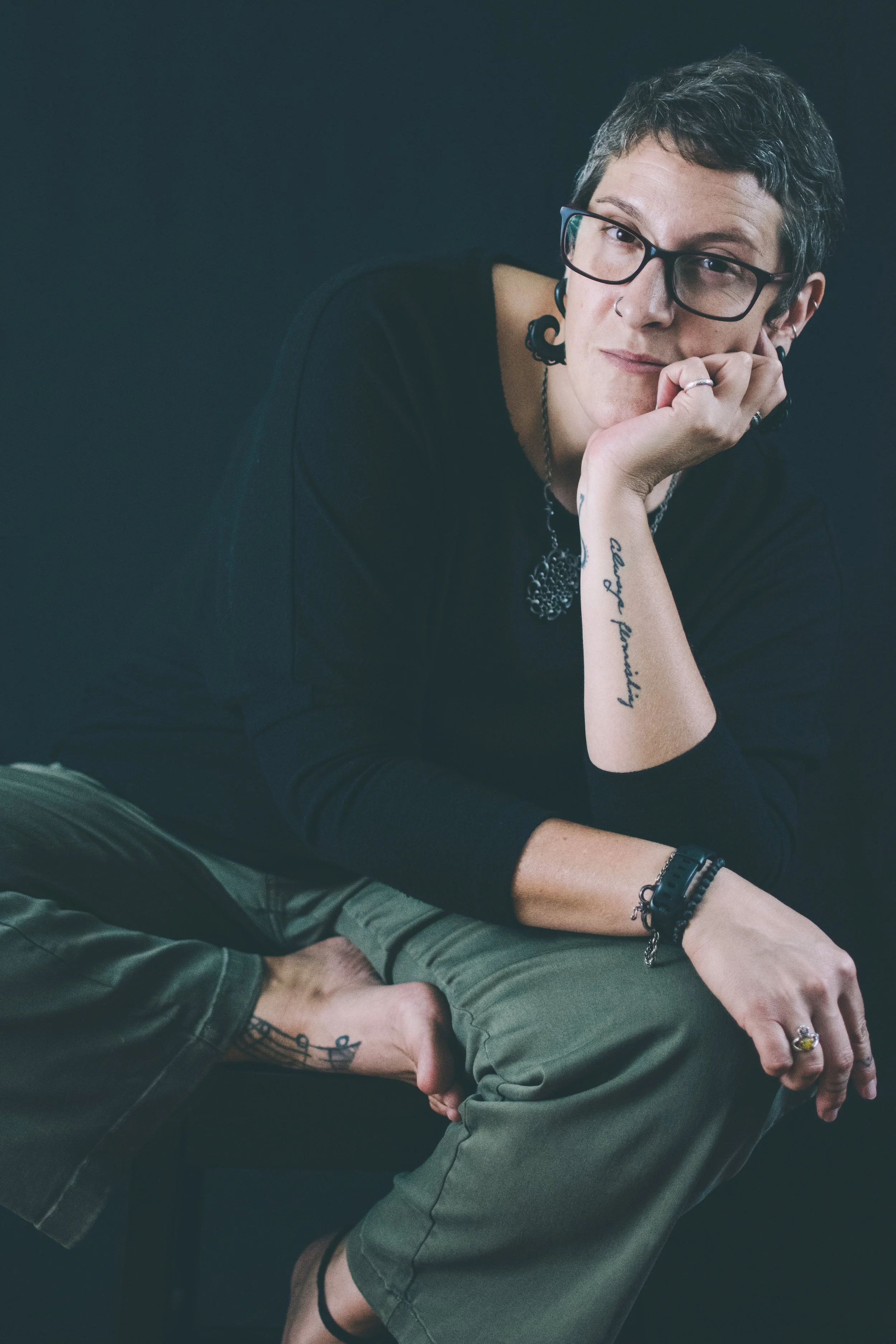 A slightly saturated image of a woman with short hair, glasses, and tattoos.