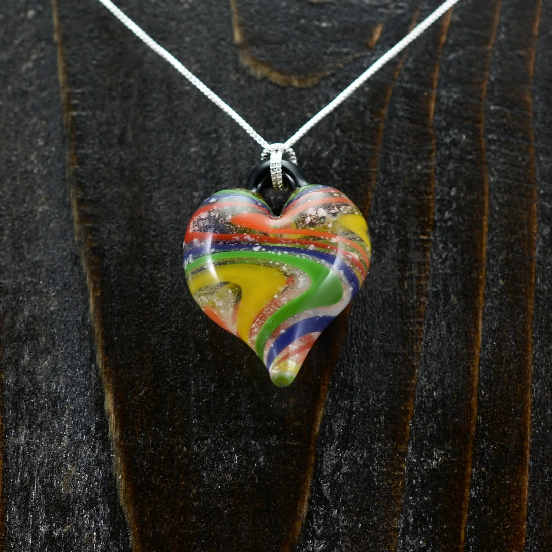 Colorful glass heart-shaped pendant necklace on dark wooden background.