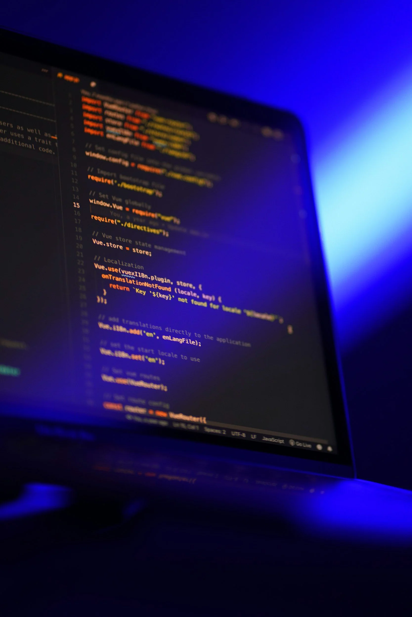 Close-up of a computer monitor displaying lines of colorful code in a dark setting with blue backlighting.