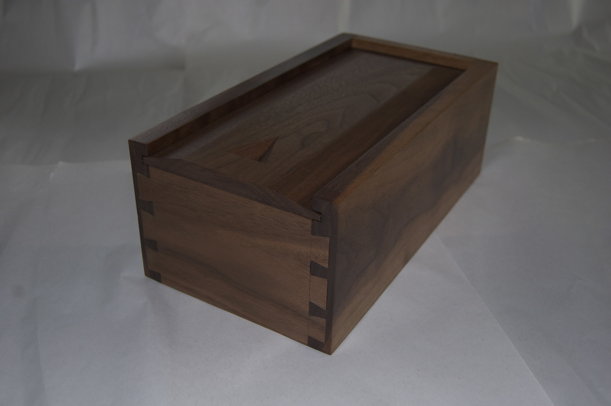 Material used for this box is walnut. Hand cut dove tails are used to join ends and sides of the box. The raised panel bottom sits in a grove, which allows it to move with changes in the season. The top is also a raised panel on three sides and slides in a grove. The top also has a carved finger pull. A satin oil and urethane finish was applied to show the grain of the wood while providing some protection from everyday use. This box is for sale for $40.00. Dimensions: 12" x 6 1/2" x 4 1/2" (Click on the picture to see how it was put together.)