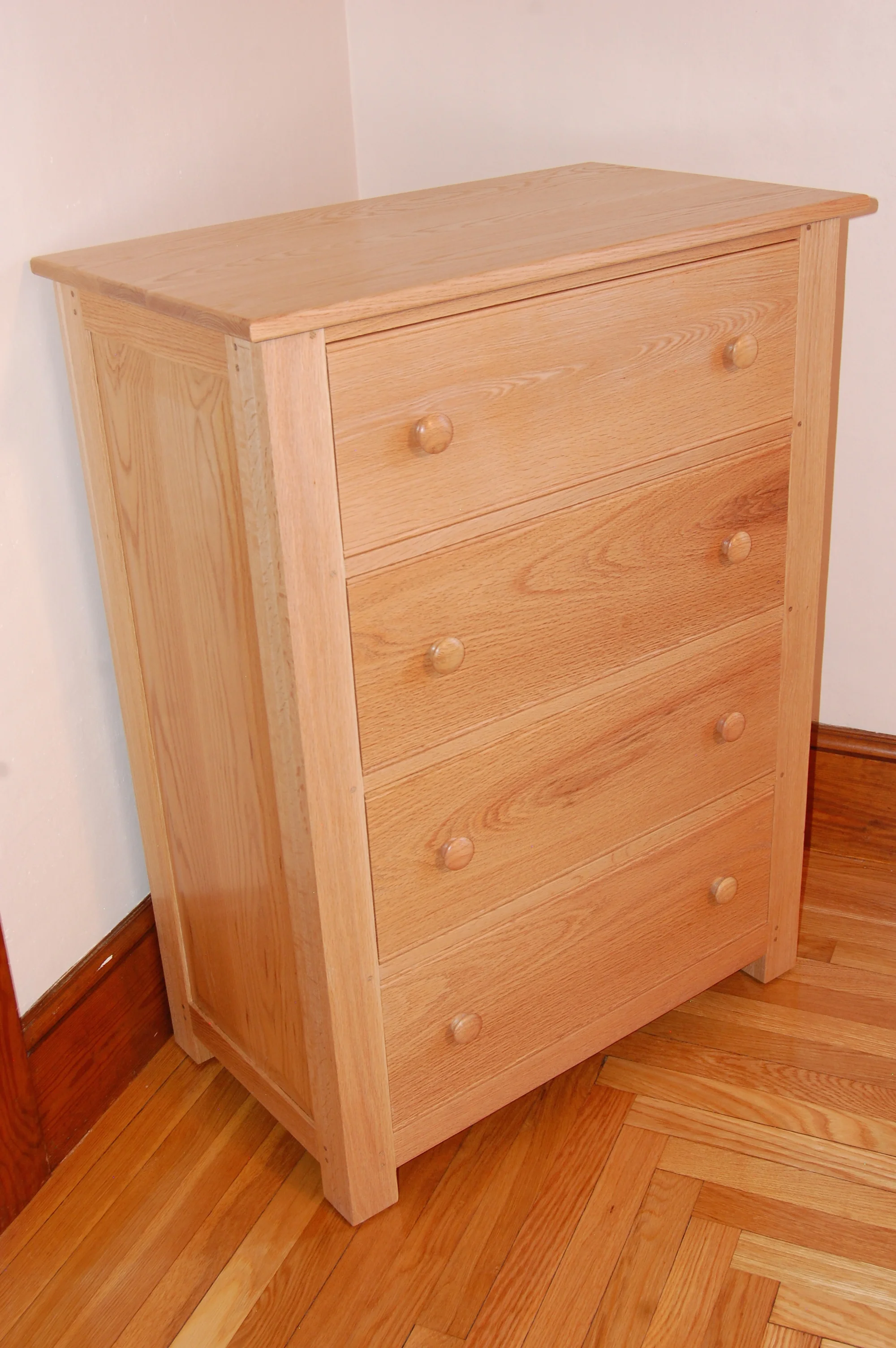 Red oak is the primary wood used for this project and 1/4" oak plywood is used for the drawer bottoms. The case is joined together with pegged mortis and tenoned joints. The case sides are raised panels, which are in grooves to allow movement during seasonal changes. Hand cut dove tails join drawer sides, backs and fronts, which are all red oak. Drawer bottoms are housed in grooves running along the drawer sides and fronts, and are screwed to drawer backs. Drawer fronts have a 1/4" bead along the top and bottom. Drawer pulls are red oak Shaker style knobs( nope I didn't turn them, bought them at a store). The case back is ship lapped panels set in a rabbit and held in place by screws. Three coats of a satin oil and urethane finish were applied, with scraping and sanding between each coat. After the final coat had dryed for several days paste wax was applied with 0000 steel wool, which gave it a very smooth feel with very little gloss. This finish allowed the natural color of the wood to show through that will darken slightly over time. This dresser was made for our grand daughter, but we would be glad to make one for you. Dimensions: 40 3/4" H x 29" W x 17" D (Click on the picture to see how it was put together.)