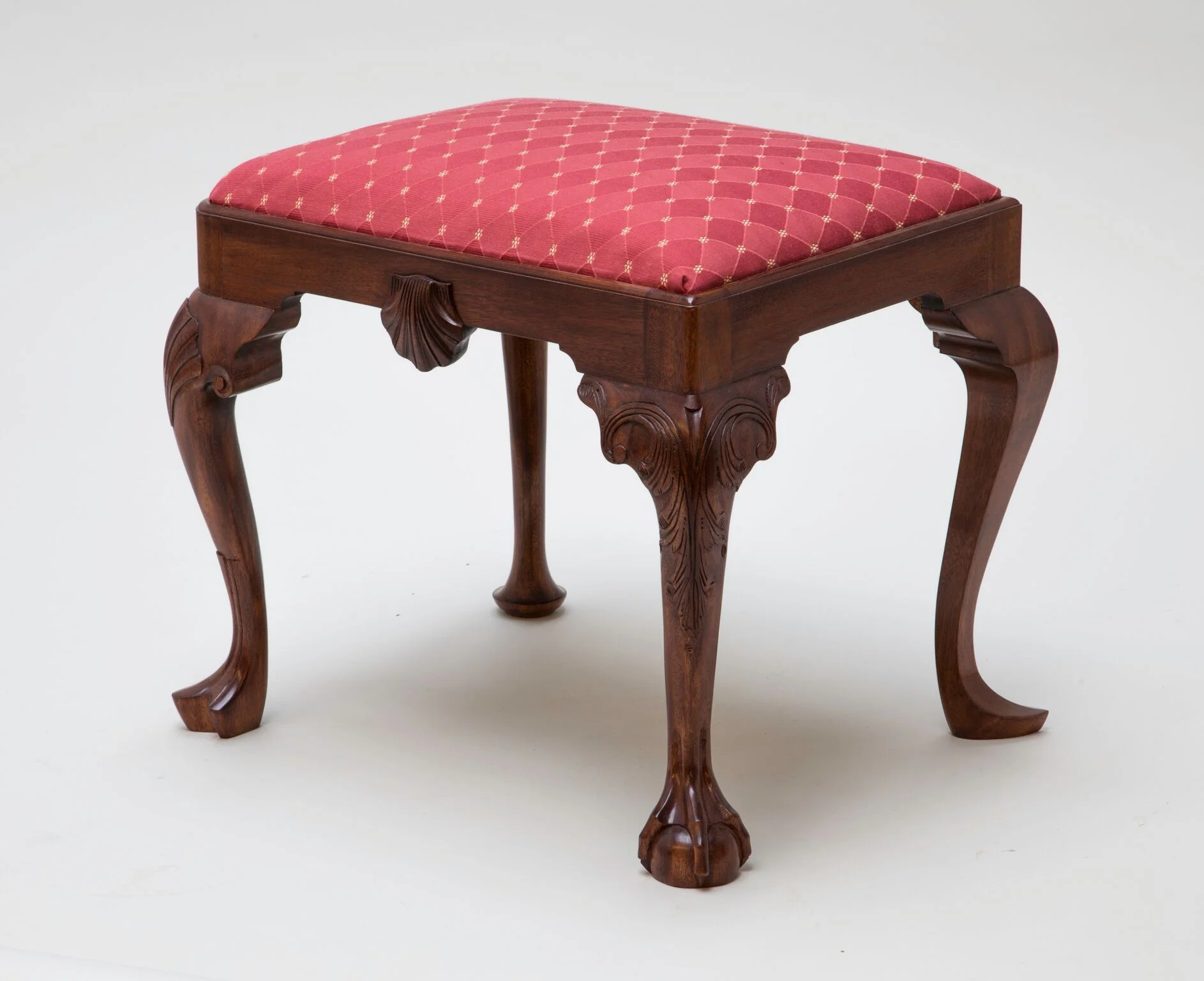 This Georgian footstool is unique in that it has four different style legs, popular for that period. Mahogany is the primary wood, pine was used for glue blocks and ash for the slip seat frame. The legs are mortised and tenoned to the rails. The shell was carved and then applied to the rail. A formula of orange dye, brown walnut dye, brown walnut pigmented stain were used to achieve the rich color. A shellac was applied by hand (French polish). Muslin, horse hair, two inch webbing, black cloth and cotton stuffing are use for the slip seat cushion. Price $1800.00. Dimension: 21" wide x 17" high x 17" deep. (Click on the picture to see how it was put together.)