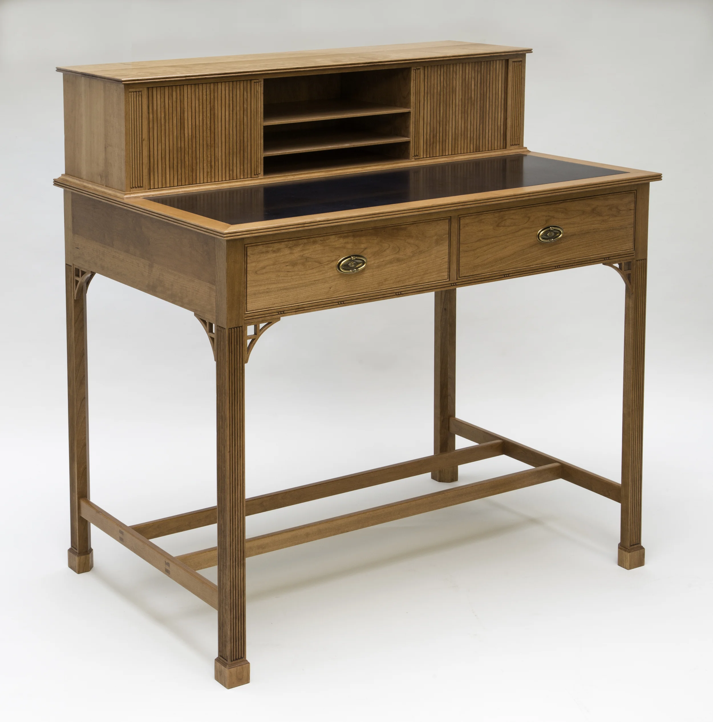 This Standing desk was designed for an open, unused space in our customer's kitchen, so that the laptop, mail, newspapers, fliers could be removed from the counters. The desk is appointed with many features found on more elegant pieces of furniture, such as reeded Marlborough legs with cuffed feet, brackets at the top of the legs, bead moldings around the writing surface and gallery top and tambour doors. Practicality and durability are also designed into this desk so that it will stand up to every day use. It is 48 inches wide, 51 inches high and 31 1/2 inches deep. The writing surface is 40 inches from the floor, which is a comfortable standing working height of our customer. The primary wood is cherry and secondary wood pine. Cherry and rose wood were used for the gallery tambour doors. The writing surface is black satin Corian. Cherry stain and an oil/urethane finish were applied to give the desk a slightly aged cherry color. A unique feature of this desk is that it can be placed anywhere in a room, against a wall, perpendicular to a wall, or in the middle of a room. Moldings continue all the way around the desk. All four legs have reeds, brackets and cuffed feet. The gallery back is a single piece of cherry veneered plywood held in place with moldings and grooves, no fasteners were used, which would detract from the appearance. This desk has found a home. However, we would be glad to work with you to create one to fit your needs. Price as seen $6000.00. We are thrilled this desk was selected to be in the Providence Journal on 10/31/2015 as part of an article on the 2015 Fine Furnishing Show in Pawtucket, RI. Click on the link below to read the article. http://providencejournal.com/article/20151031/ENTERTAINMENTLIFE/151039961
