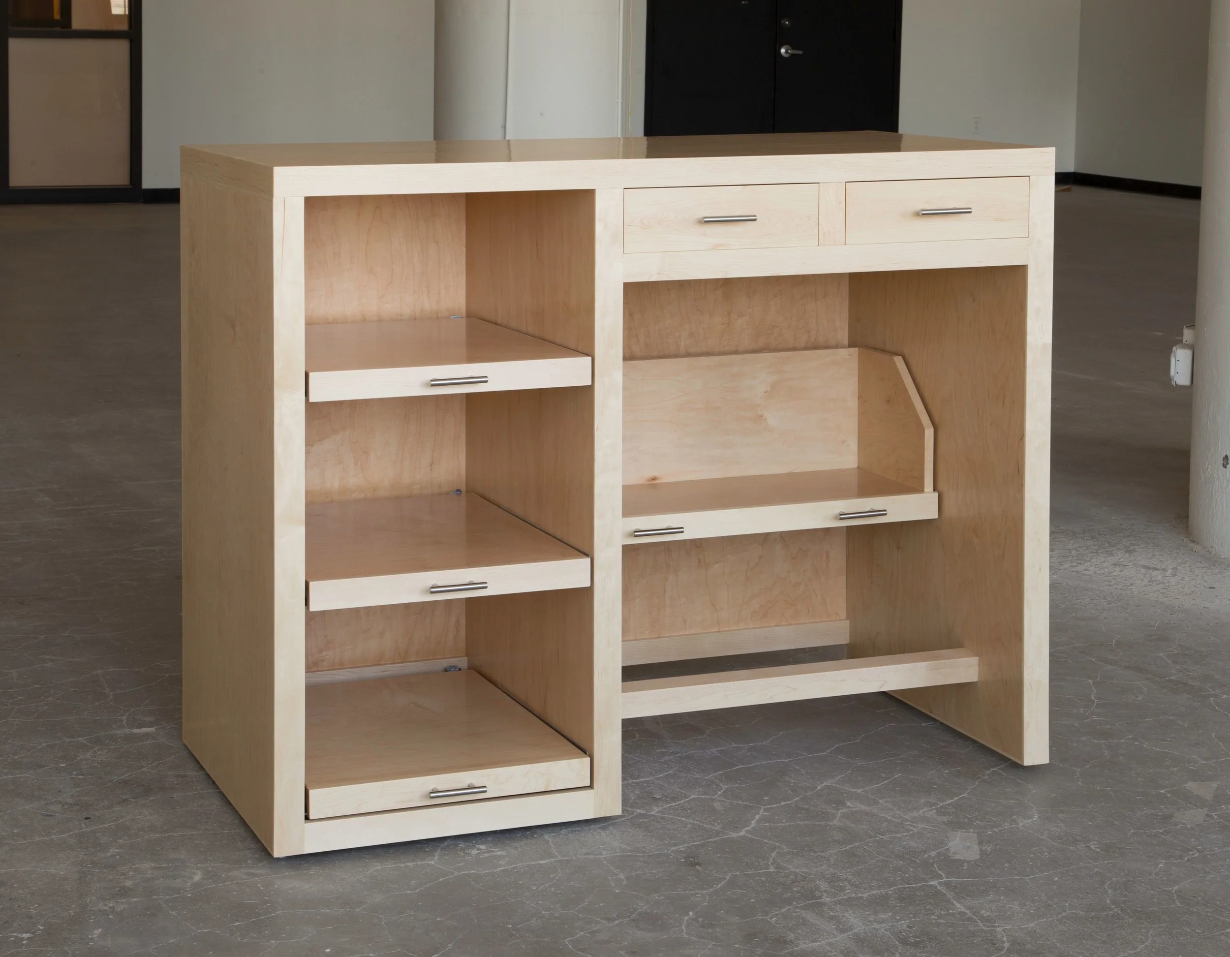 This is a very unusual piece for us. The client has office furniture from a big box store (whose name I won’t mention) and the husband wanted a stand up desk to use for his photography hobby. They could not find anything that would go with their existing office furniture, so they asked us to come up with something. Here it is, a stand up desk made with Maple plywood and hardwood, finished with lacquer, which came close to their existing office furniture color. The 3 pull out shelves on the left side are for a printer, scanner and enlarger. The pull out shelf on the right is a bookshelf for photography books. Two drawers above that are for miscellaneous photography stuff. There is also a footrest on the right side so that he can change position while working. The desk is 57” long, 46” high (the client is 6’ 4” tall) and 27” deep.