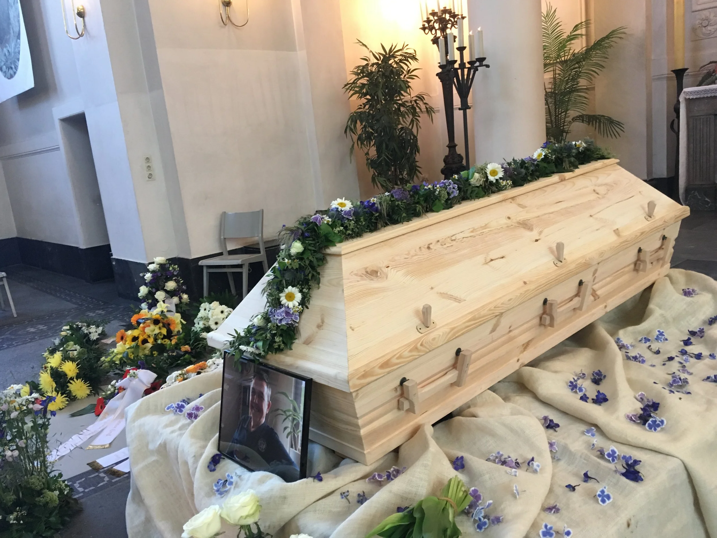Ein Holzsarg steht auf einem Tisch, umgeben von Blumen.
