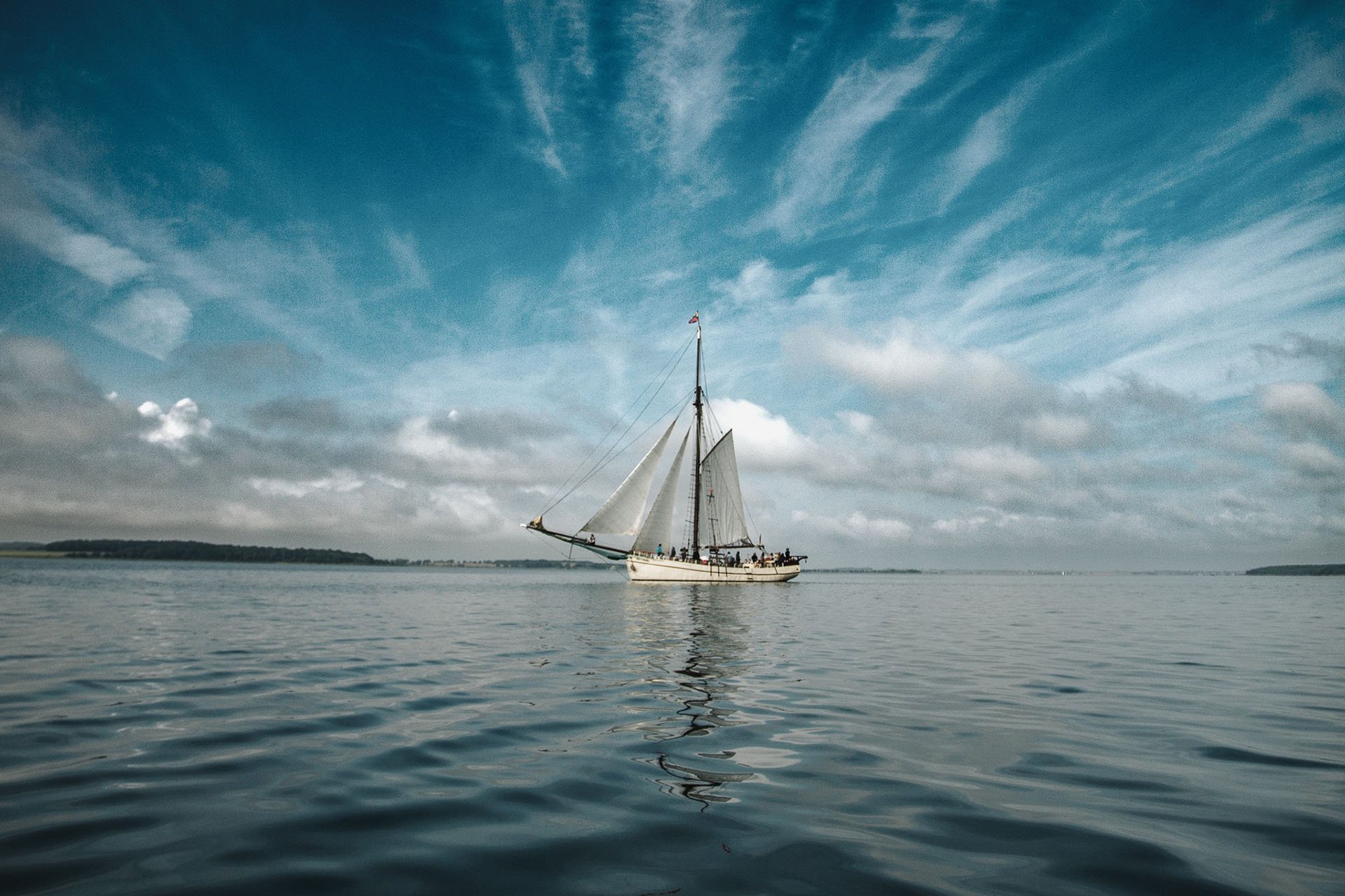 Segelschiff auf ruhigem Wasser mit Himmel und Wolken im Hintergrund.