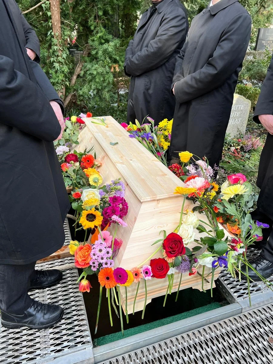 Mit Blumen geschmückter Sarg bei einer Erdbestattung