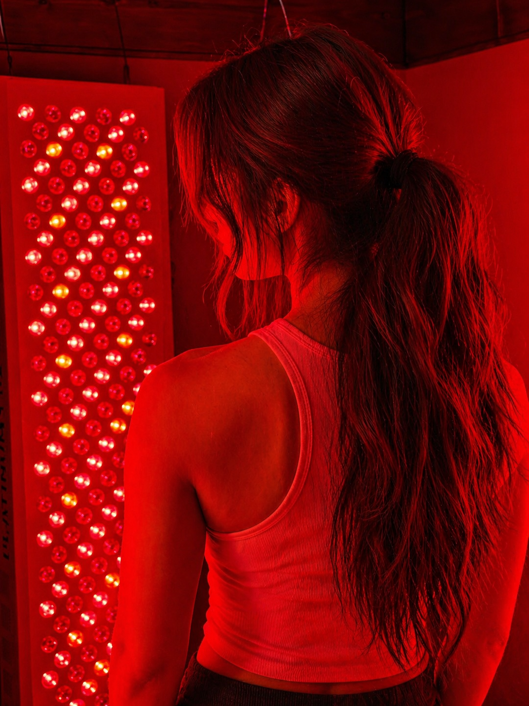 Back of a woman with long hair, illuminated in red light, standing in front of a red-lit panel.