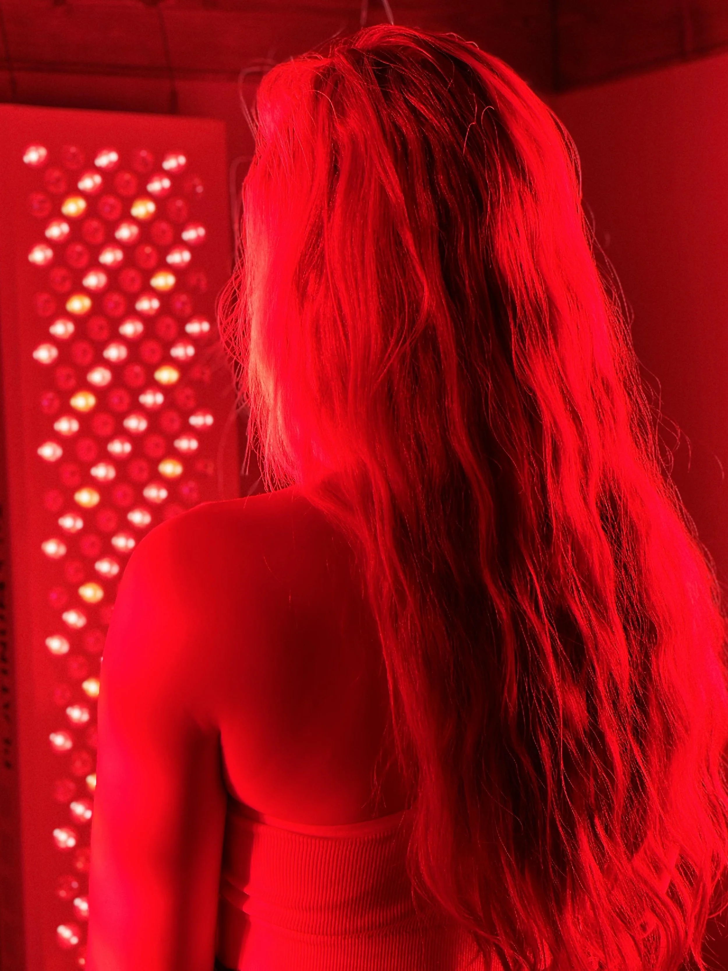 Back of a woman with long hair, illuminated in red light, standing in front of a red-lit panel.